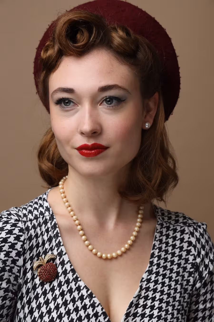 Frau im Retro-Stil mit roten Lippen, Perlenkette, rotem Hut und schwarz-weißem Kleid mit Hahnentrittmuster.