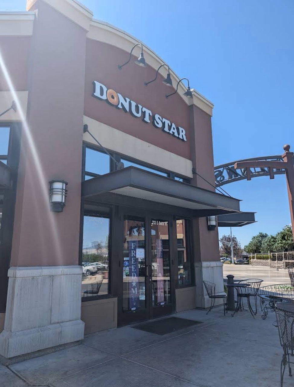 Exterior view of Donut Star shop entrance with outdoor seating and clear blue sky.