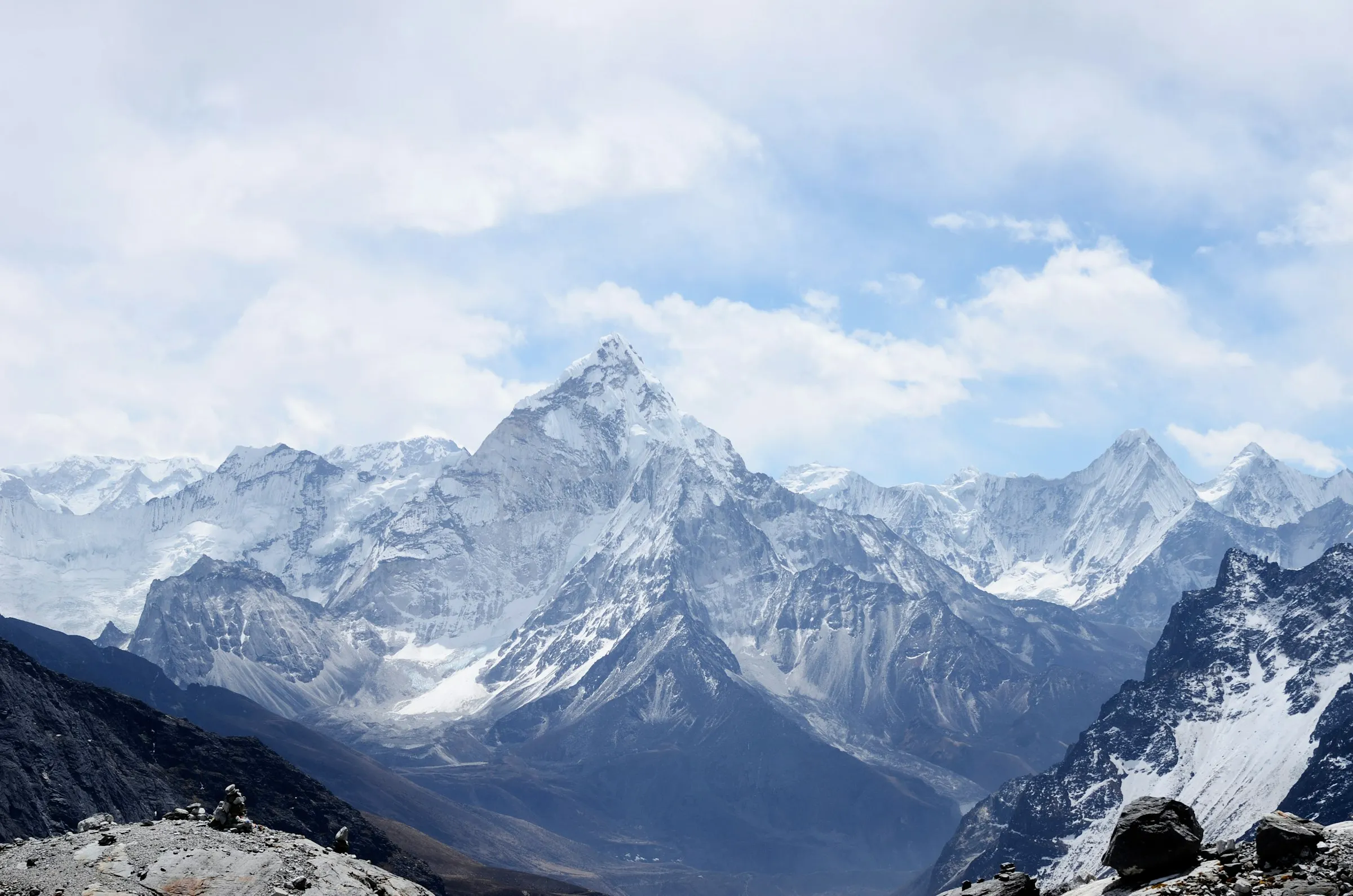 Snow-covered jagged mountain peaks under a partly cloudy blue sky with rocky foreground.