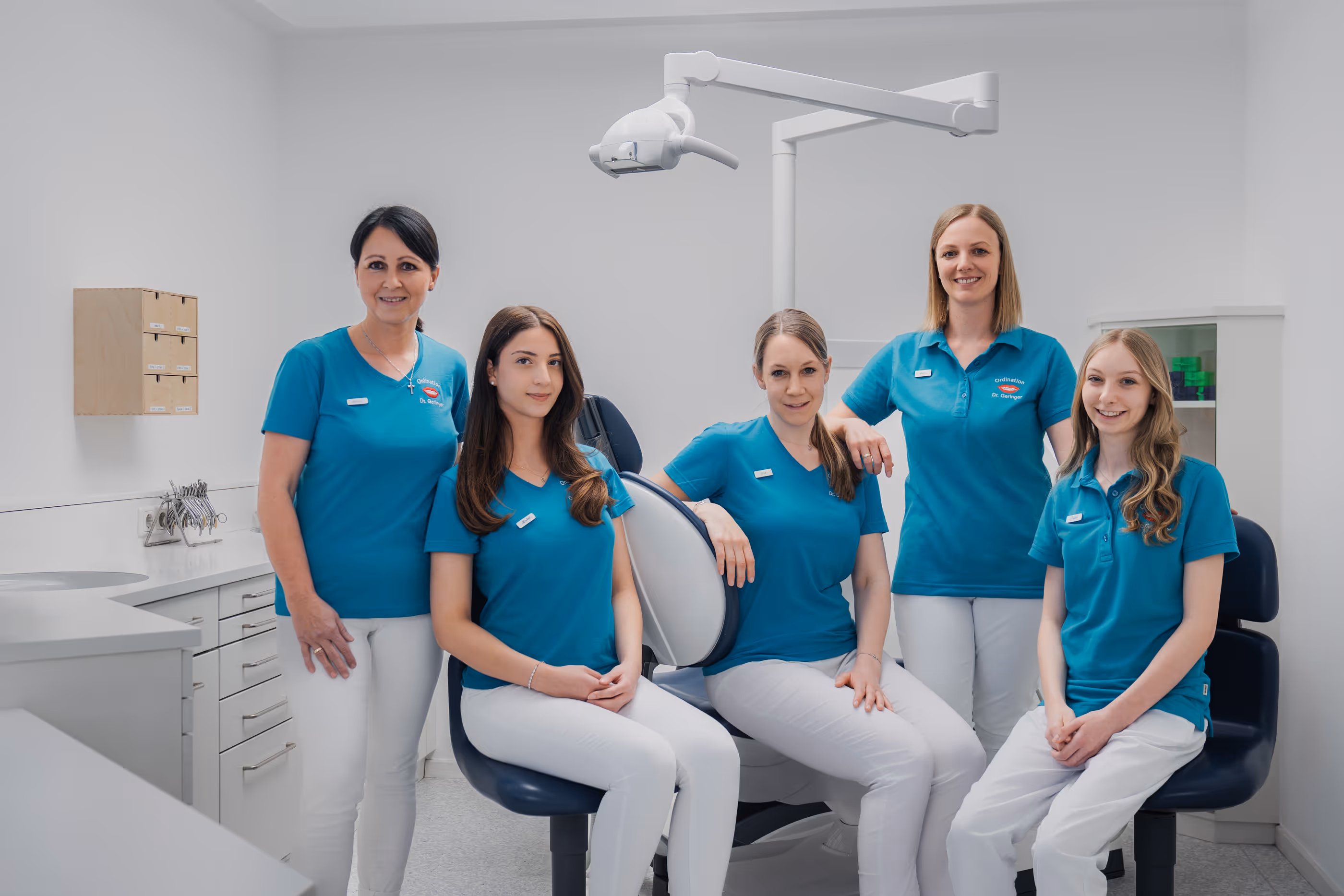 Fünf Frauen in blauen Polohemden und weißen Hosen in einer Zahnarztpraxis posieren lächelnd.