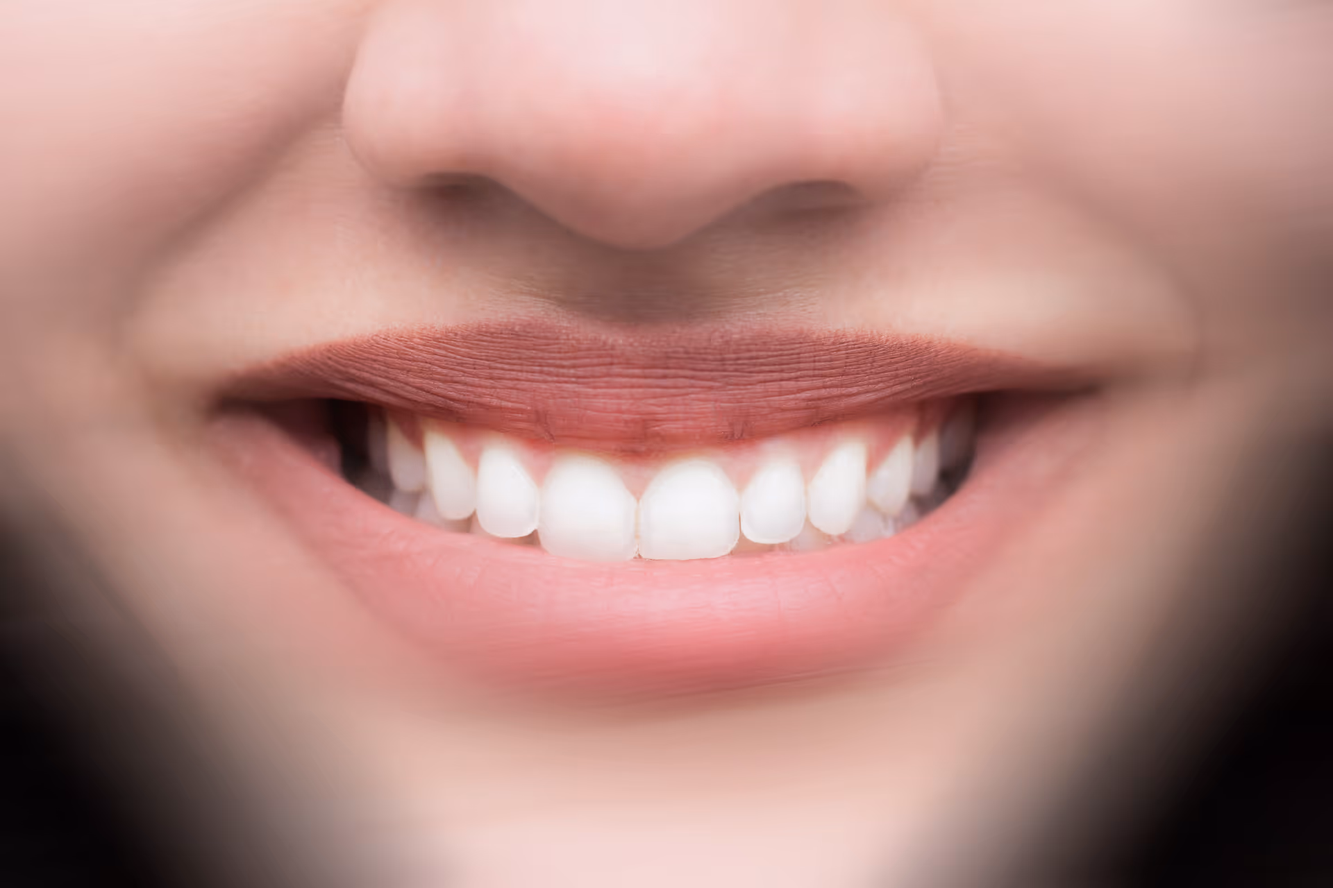 Lächelnder Mund mit gesunden weißen Zähnen und dezentem Lippenstift.