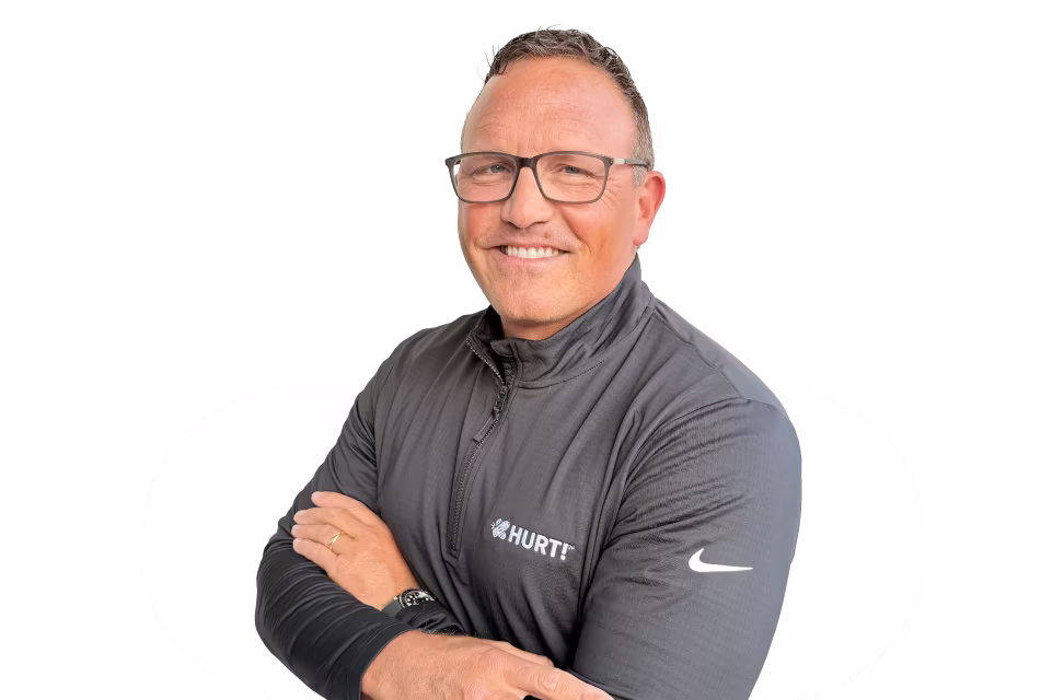 Smiling middle-aged man wearing glasses and a dark zip-up jacket with HURT logo and Nike swoosh, arms crossed.