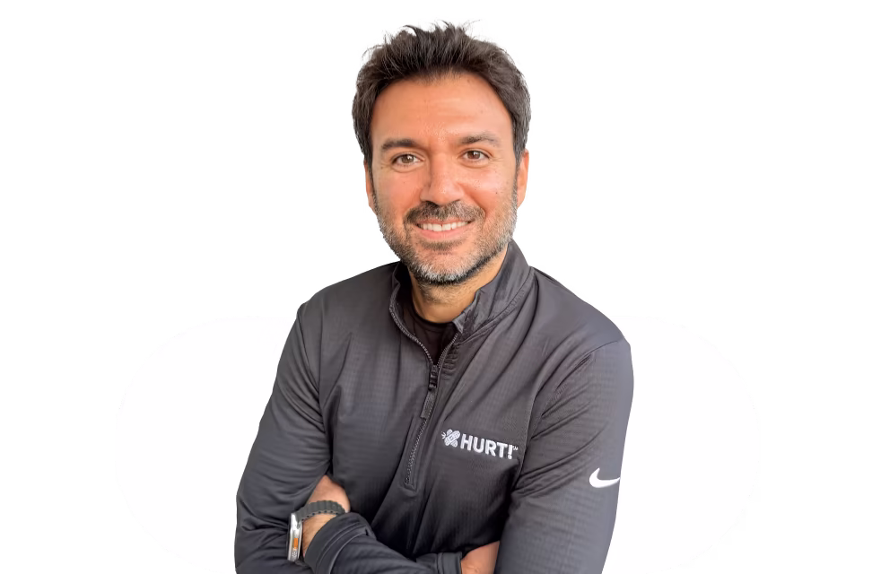 Smiling man with crossed arms wearing a black zip-up jacket with HURT! logo and Nike swoosh on sleeve.