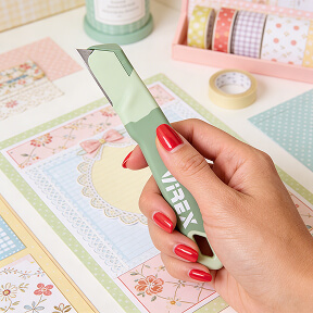 Ženska roka uporablja VIREX HOME nož pri izdelavi scrapbooka