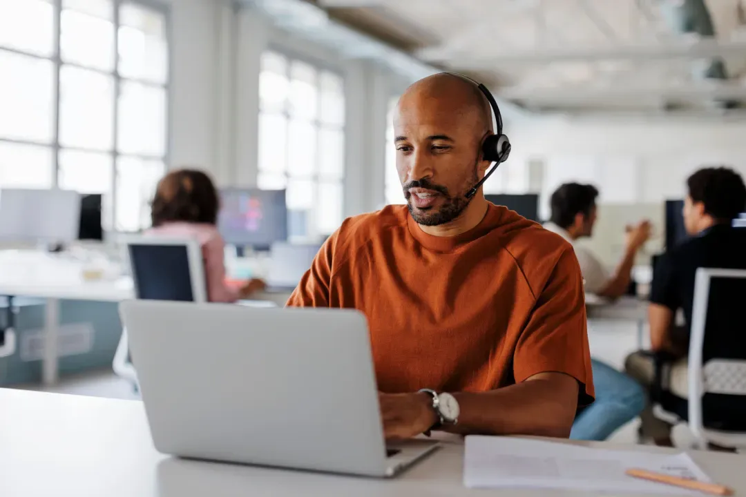 Telesales rep with a headset working on his laptop