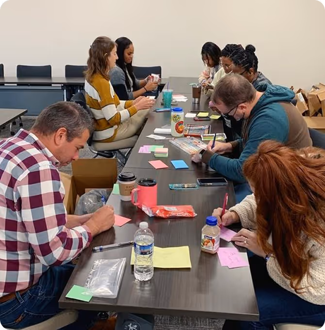Seven people sitting around a table writing on colorful sticky notes in a meeting room.