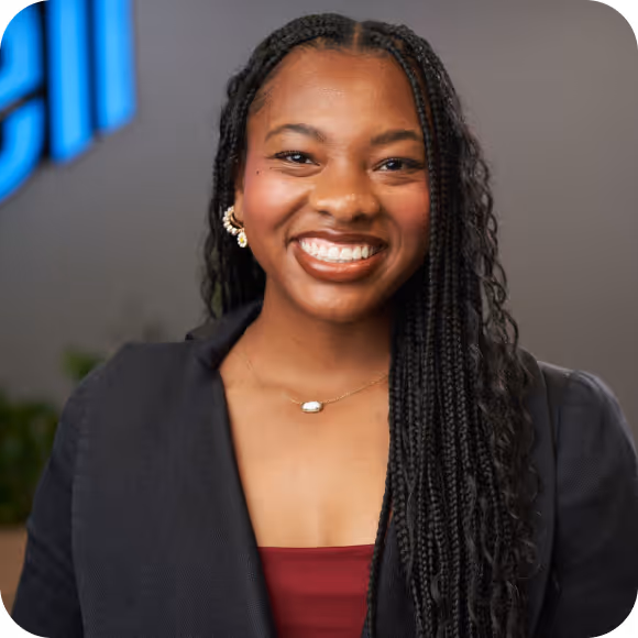 Smiling woman with long braided hair wearing earrings, necklace, and a black blazer over a red top.
