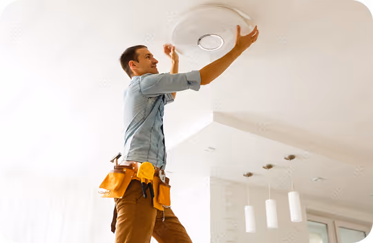 Technician installing or inspecting a ceiling smoke detector in a home's living area.