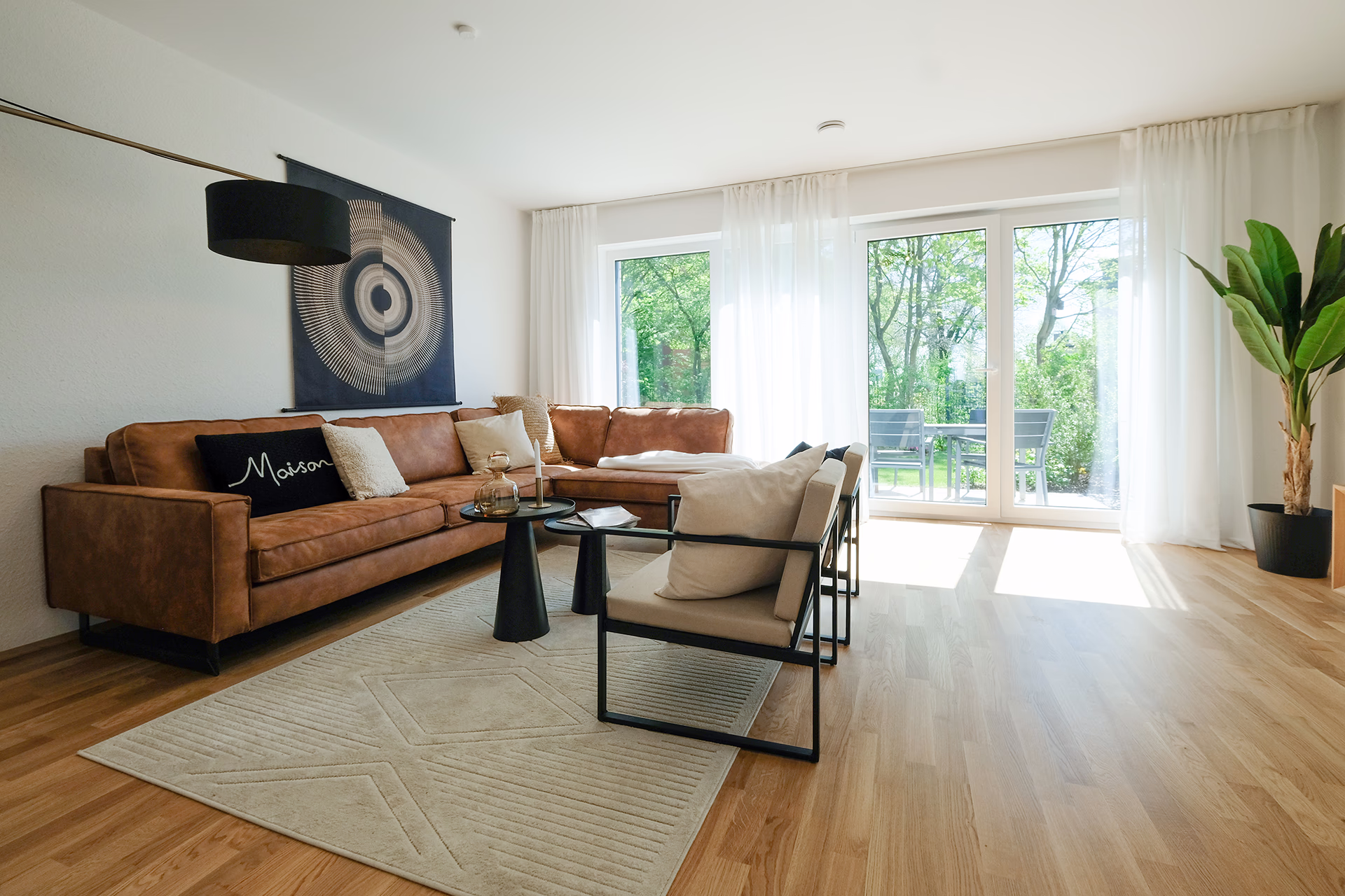 Neubauprojekt Leverkusen Steinbüchel: Modernes Wohnzimmer mit einem braunen Ecksofa, einem blauen Sessel mit gemusterter Decke, schwarzer Stehlampe, runder Wandkunst und Essbereich mit Pendelleuchten.