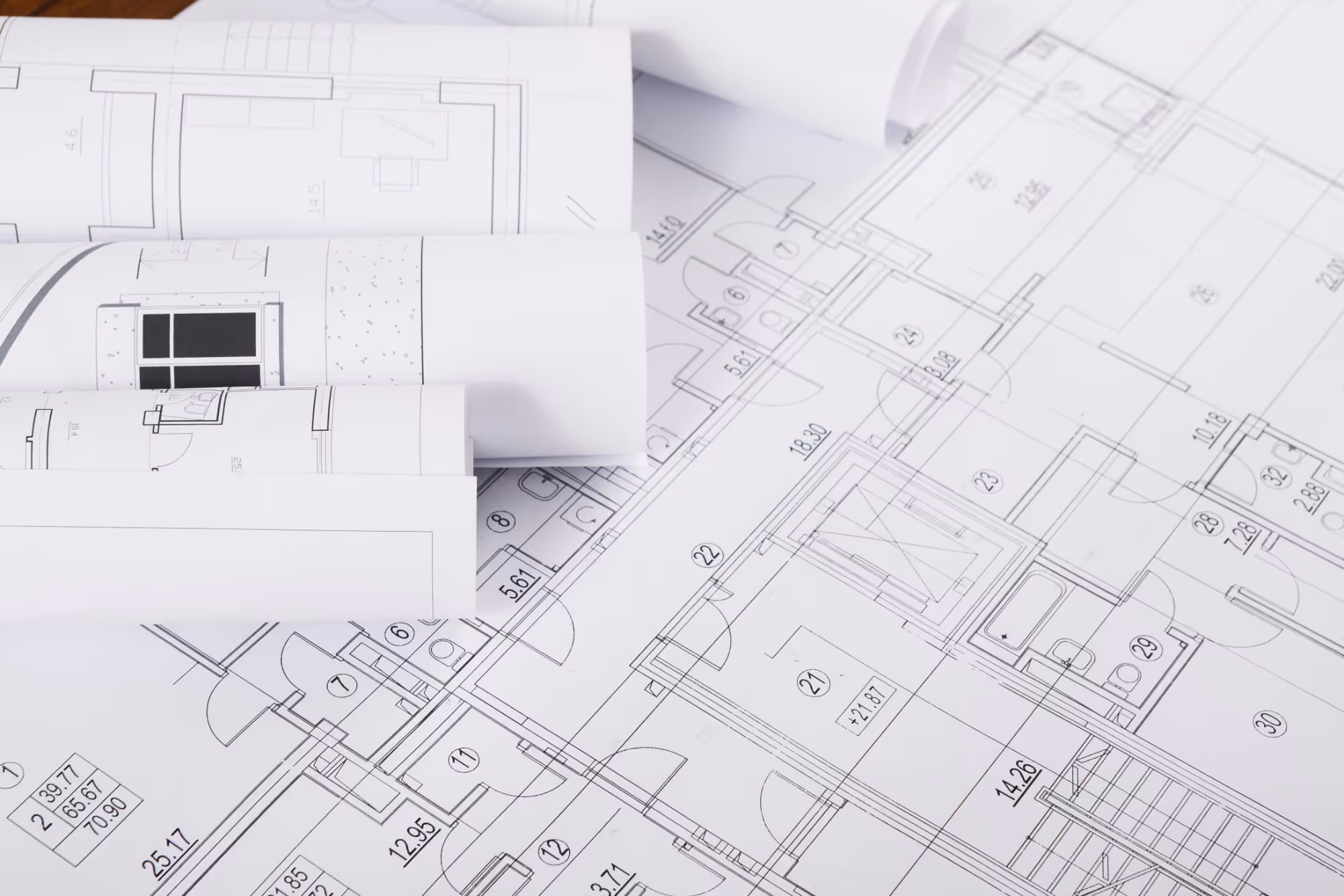 Architectural building blueprints and floor plans spread out and partially rolled on a table.