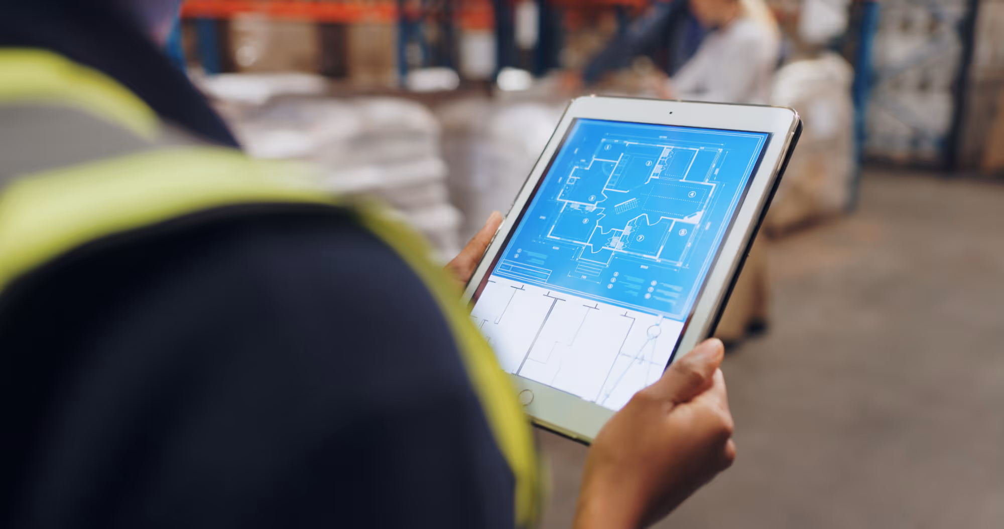 Person in a safety vest holding a tablet displaying a digital architectural blueprint.