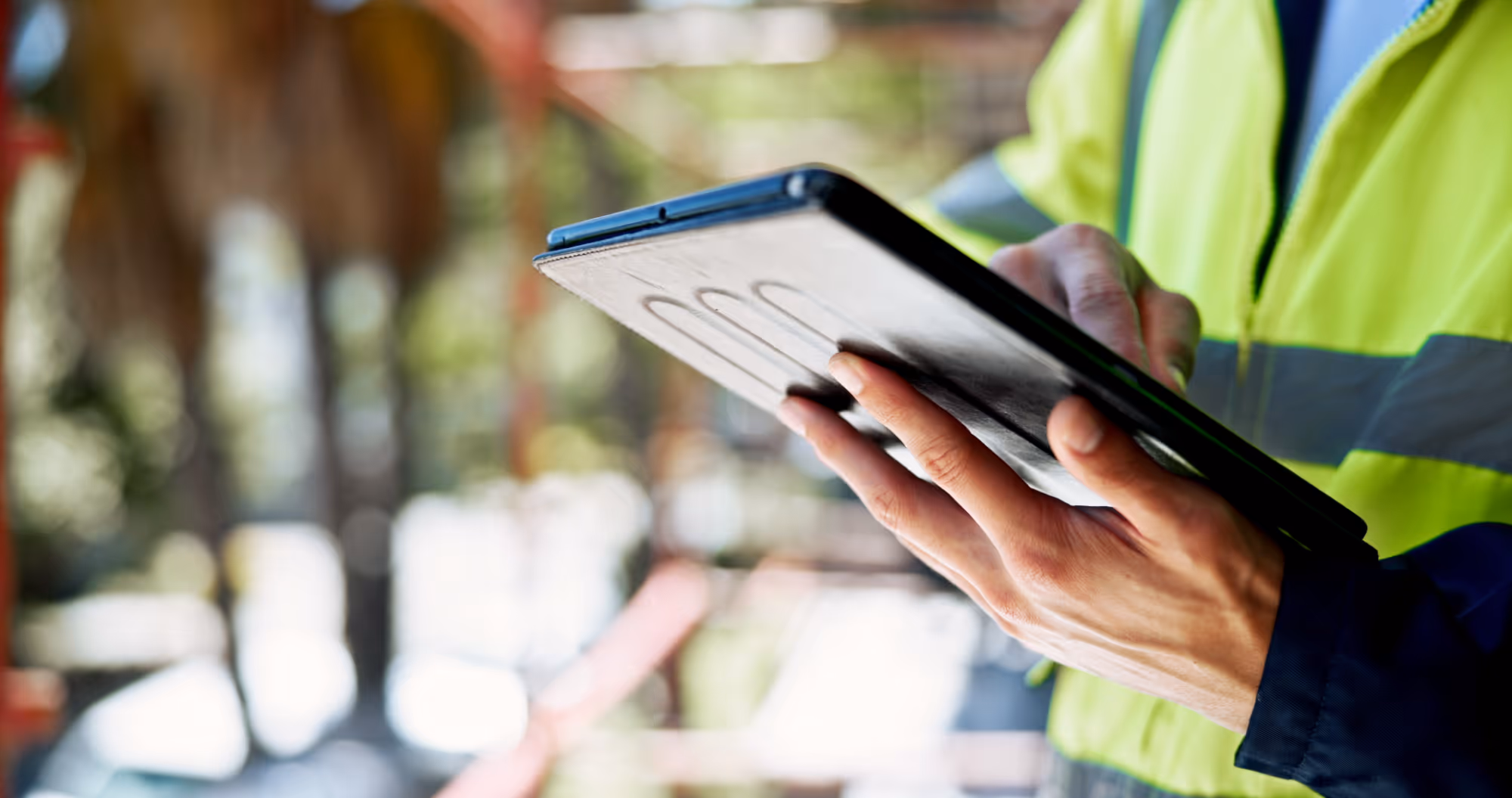 Construction worker wearing a yellow safety vest using a digital tablet at a worksite.