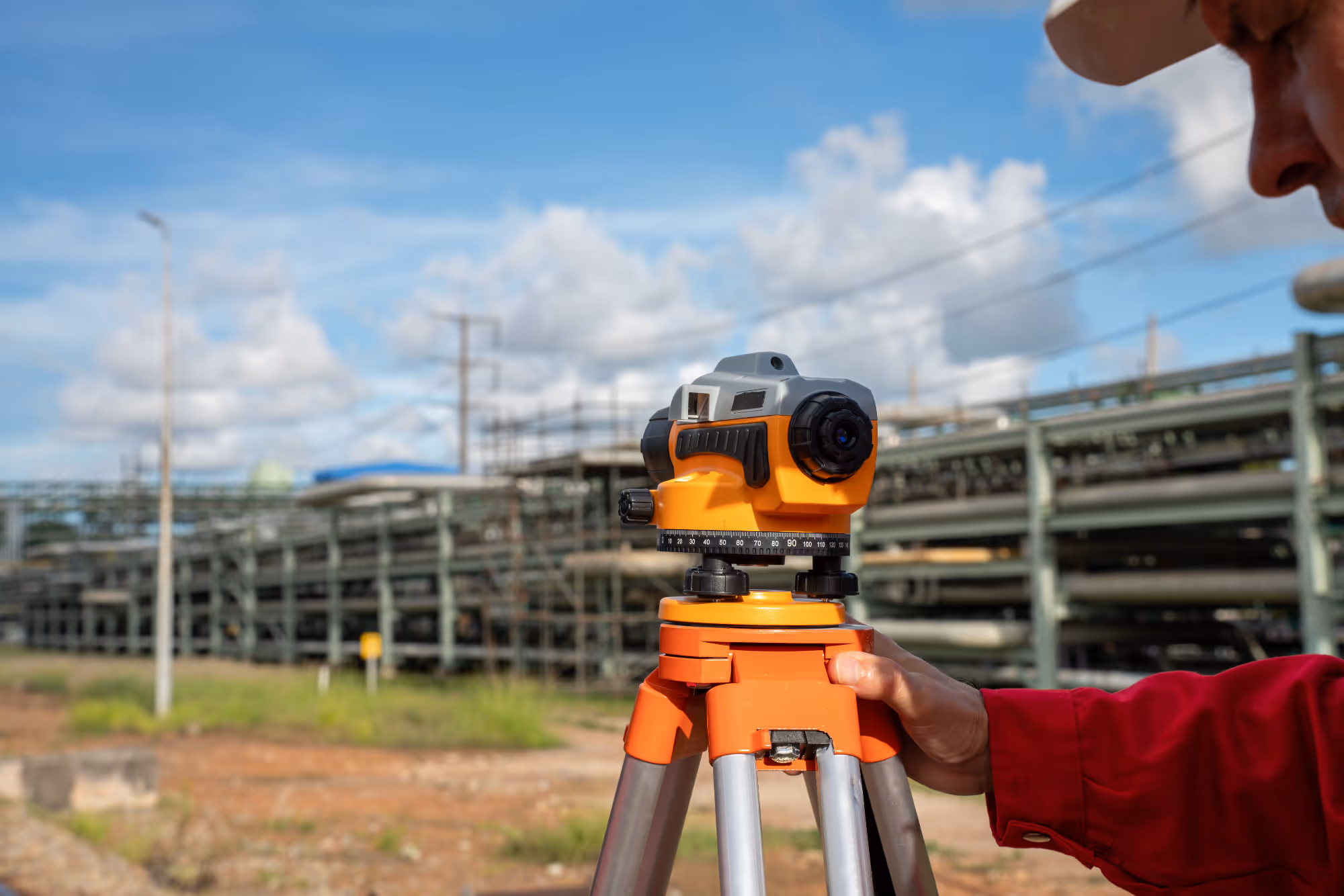Surveyor adjusting an orange optical level tool on tripod at an outdoor construction site.