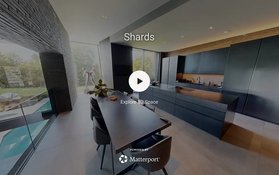 Modern kitchen with a long black dining table, black chairs, dark cabinetry, large windows, and a view of a garden and pool.