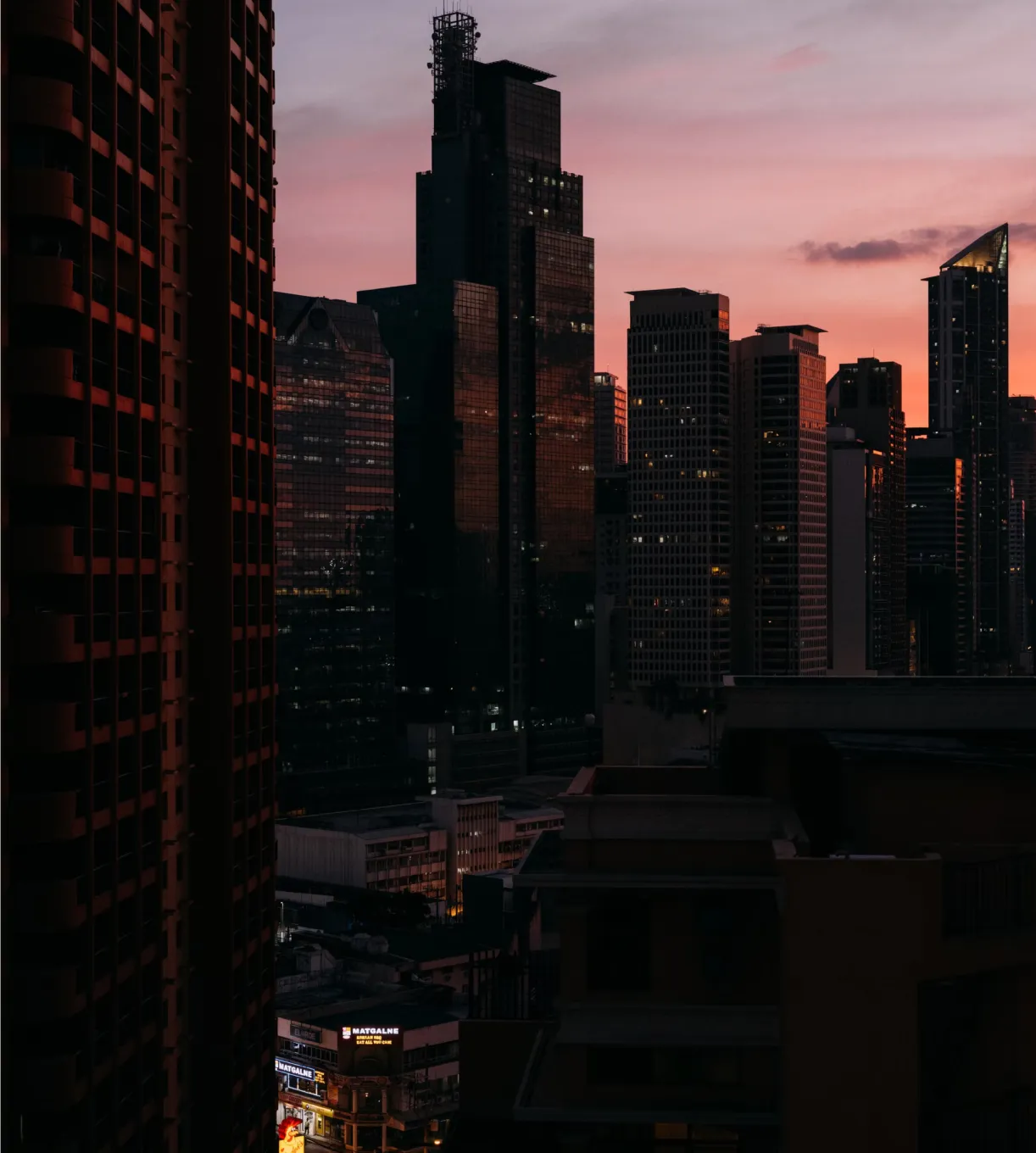 City skyline at dusk with tall skyscrapers reflecting the pink and purple hues of the sunset.