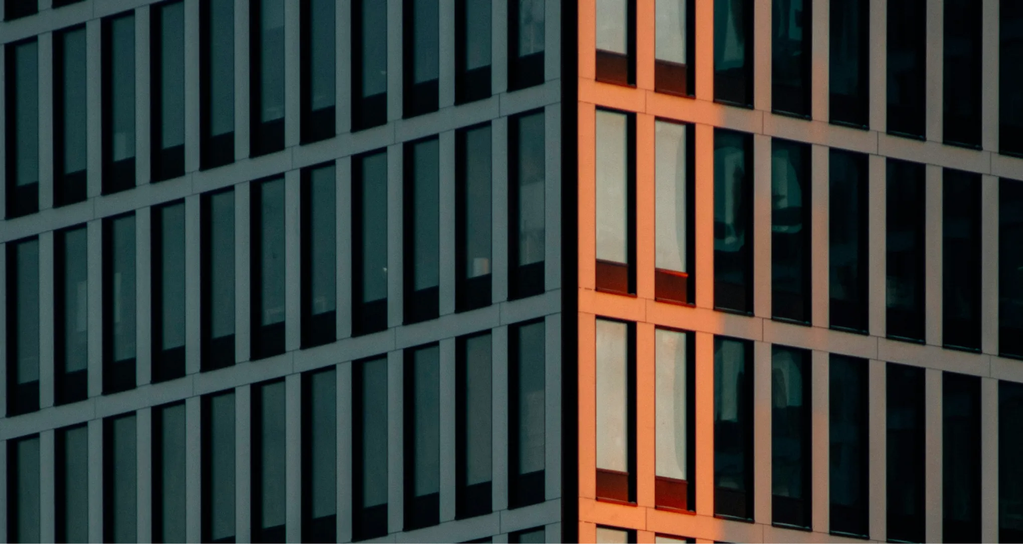 Corner of a modern office building with dark window panels and one side illuminated in orange light.