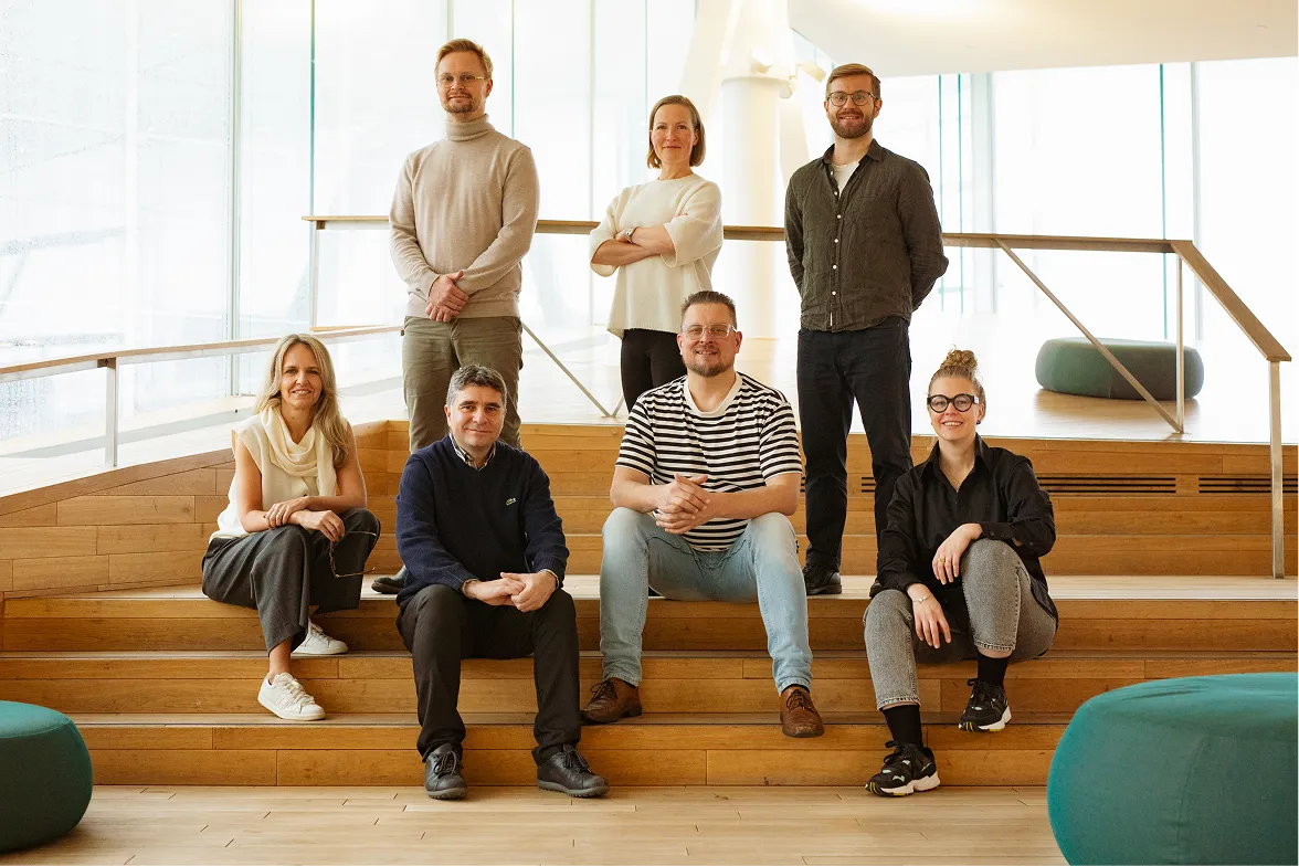 Group of seven people posing on wooden steps in a bright modern indoor space.