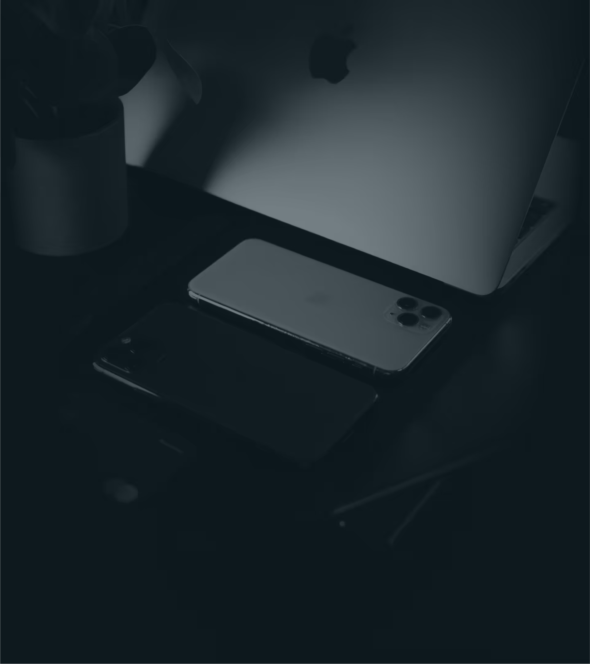 iPhone and MacBook on a dark desk with a plant