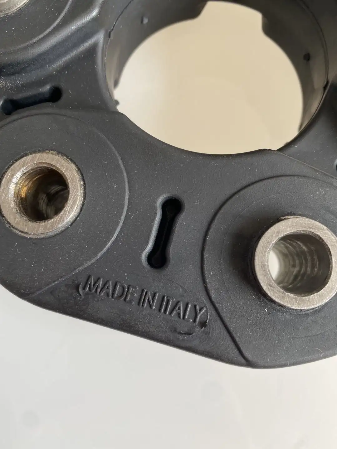 Close-up of a black mechanical part with metal inserts and 'MADE IN ITALY' embossed text.