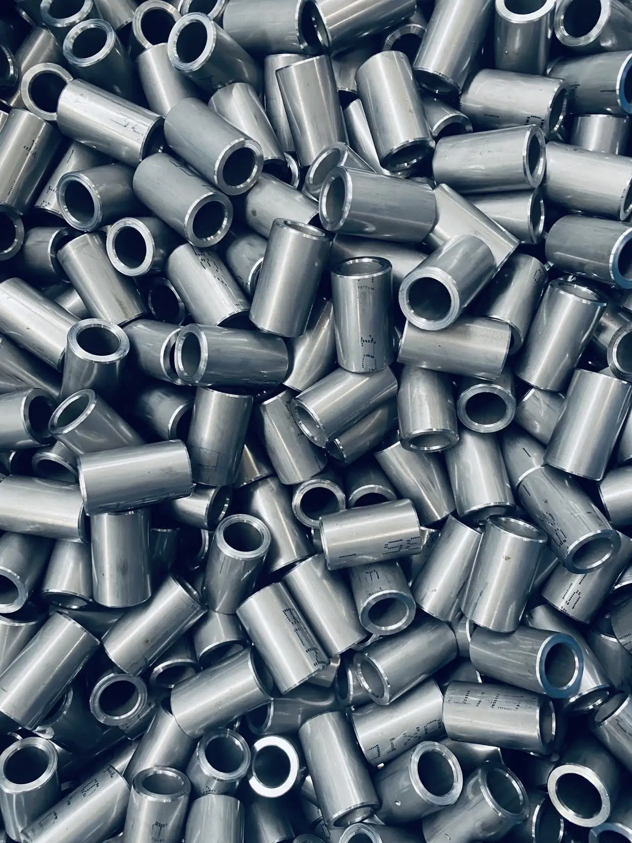 Pile of shiny metal cylindrical tubes with hollow centers and smooth surfaces.