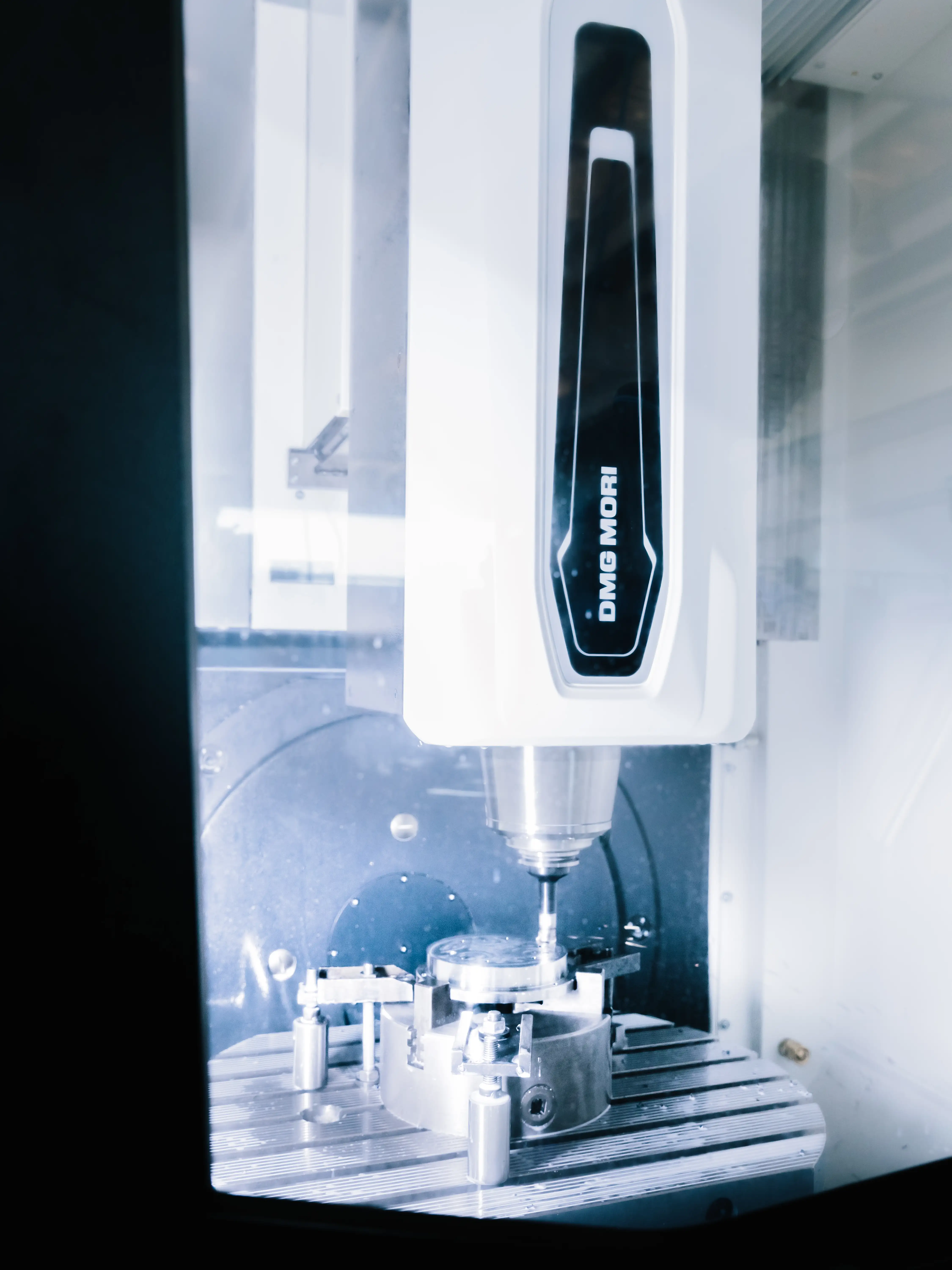Close-up of a DMG MORI CNC milling machine working on a metal circular part inside a protective enclosure.