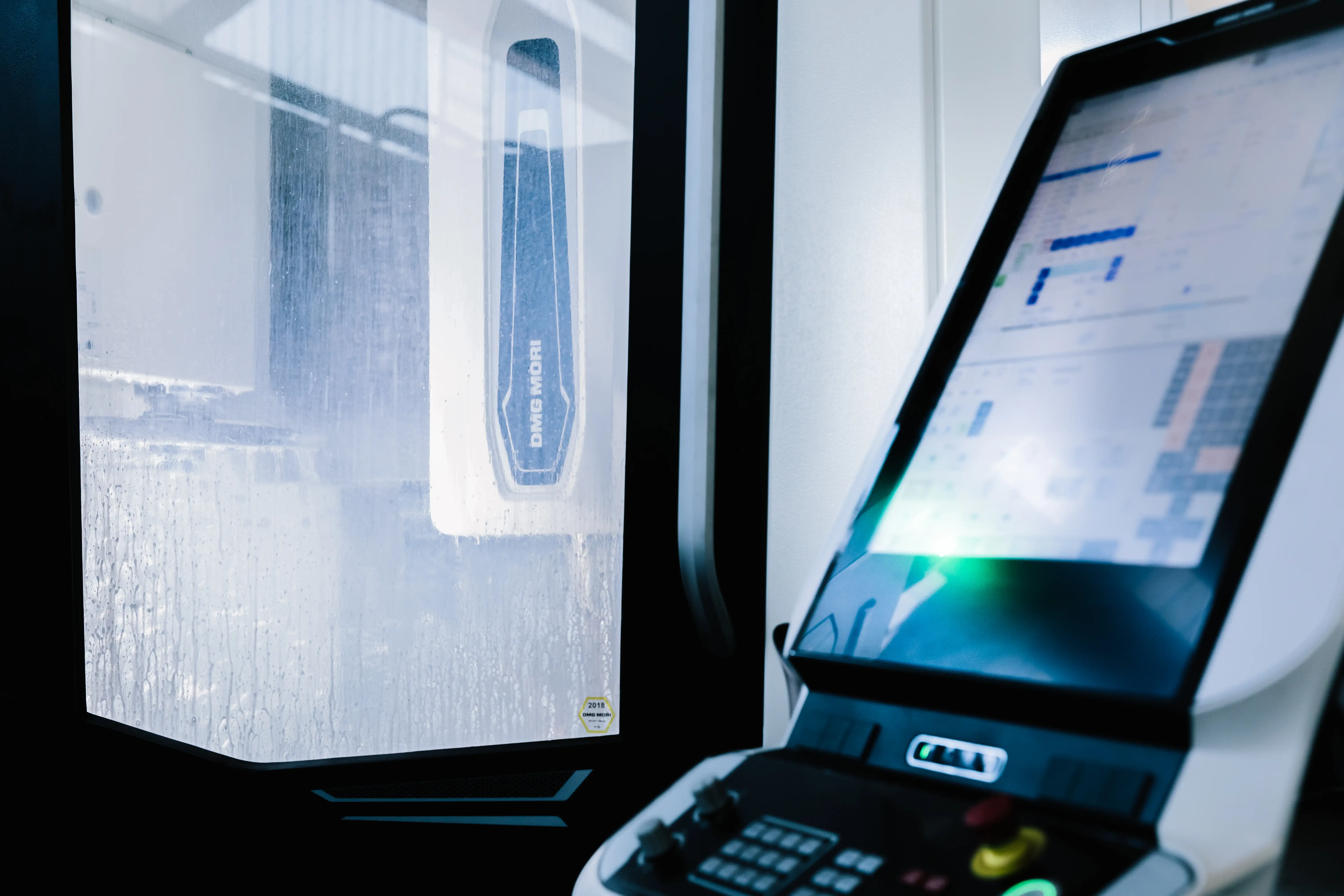 Close-up of a CNC machine and its digital control panel with a glowing green light.