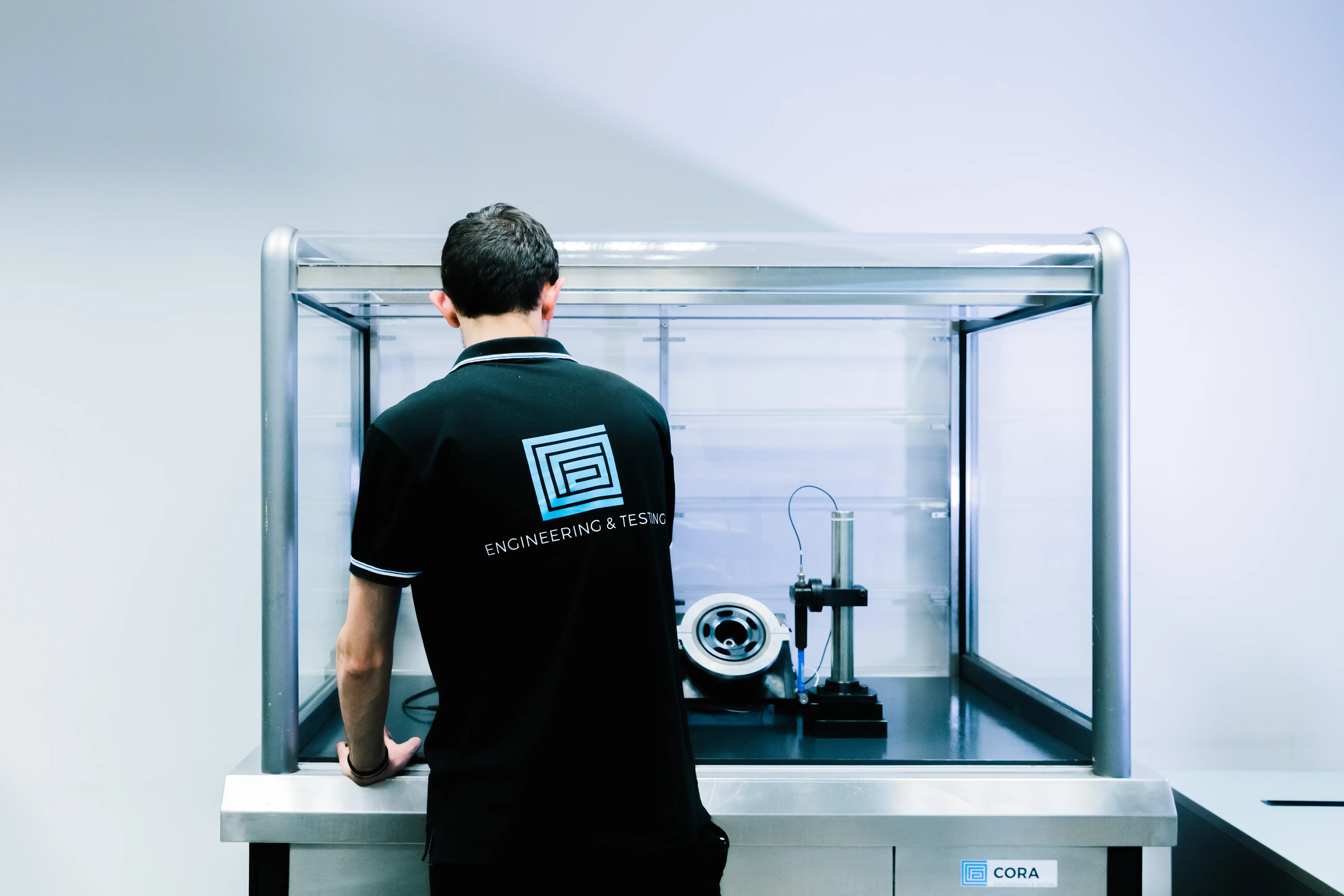 Person in a black shirt labeled Engineering & Testing working with equipment inside a transparent enclosure.