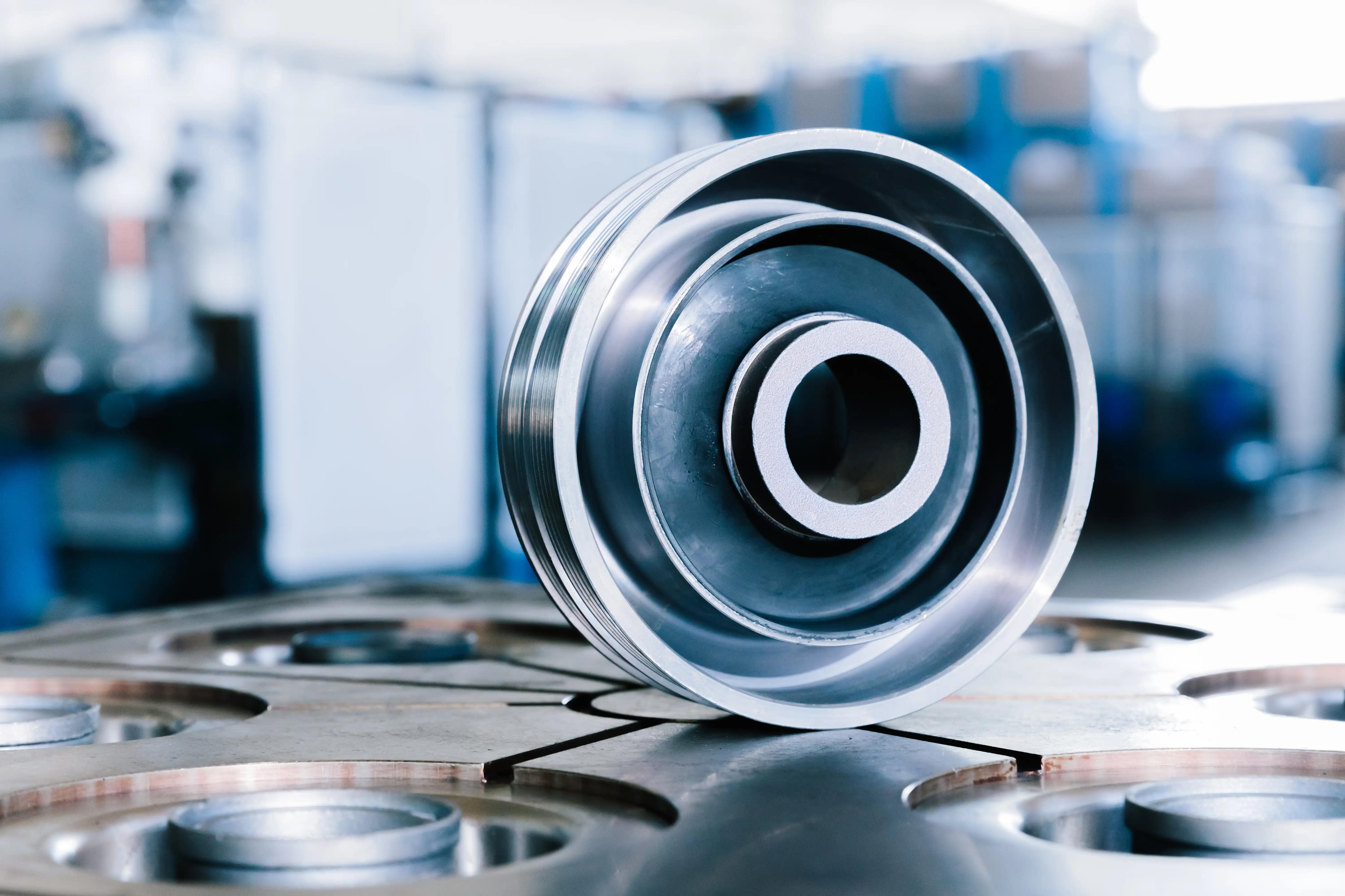 Close-up of a shiny metal pulley with grooves resting on an industrial metal surface.