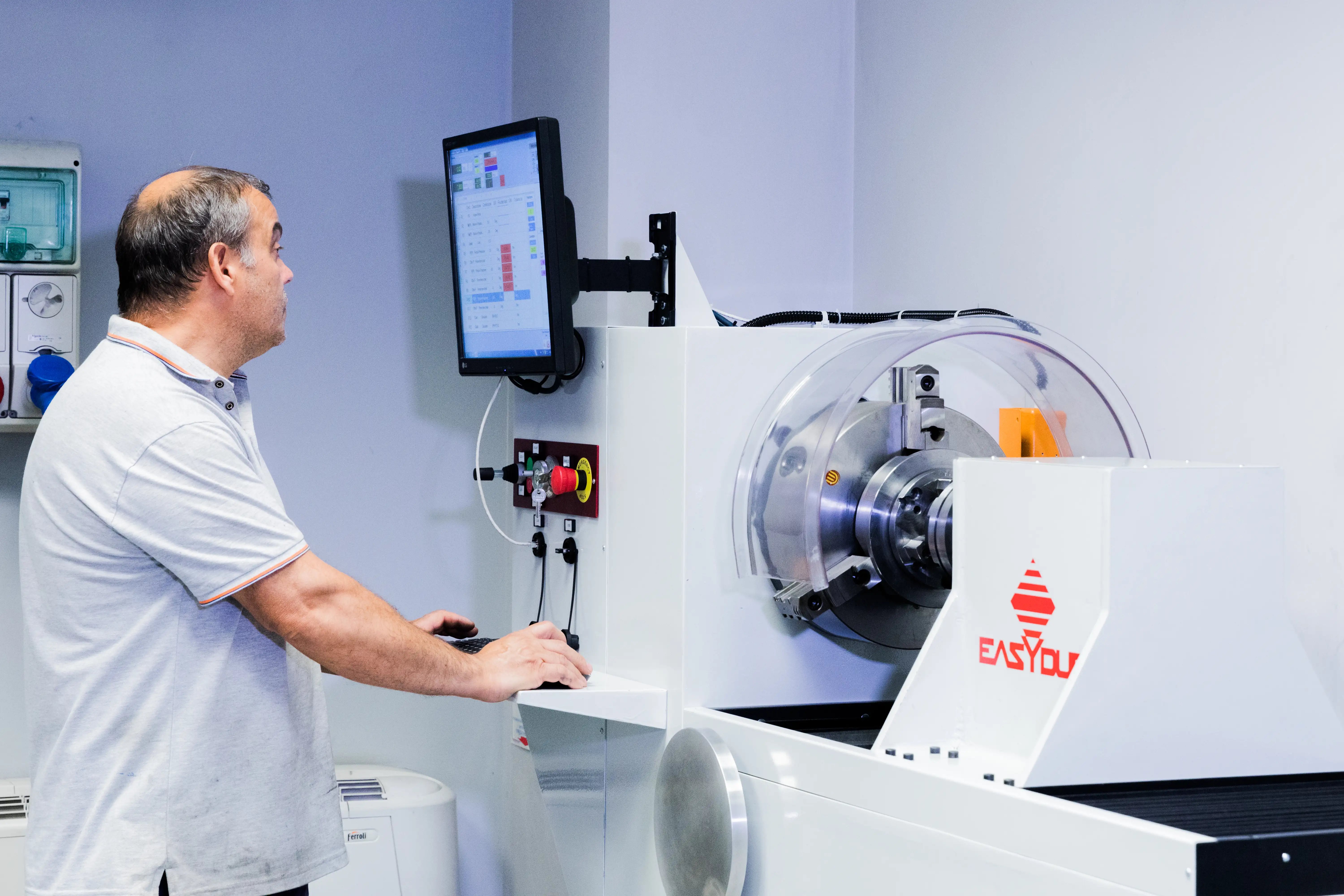 Man operating a white Easycut machine while looking at its monitor in a clean industrial room.