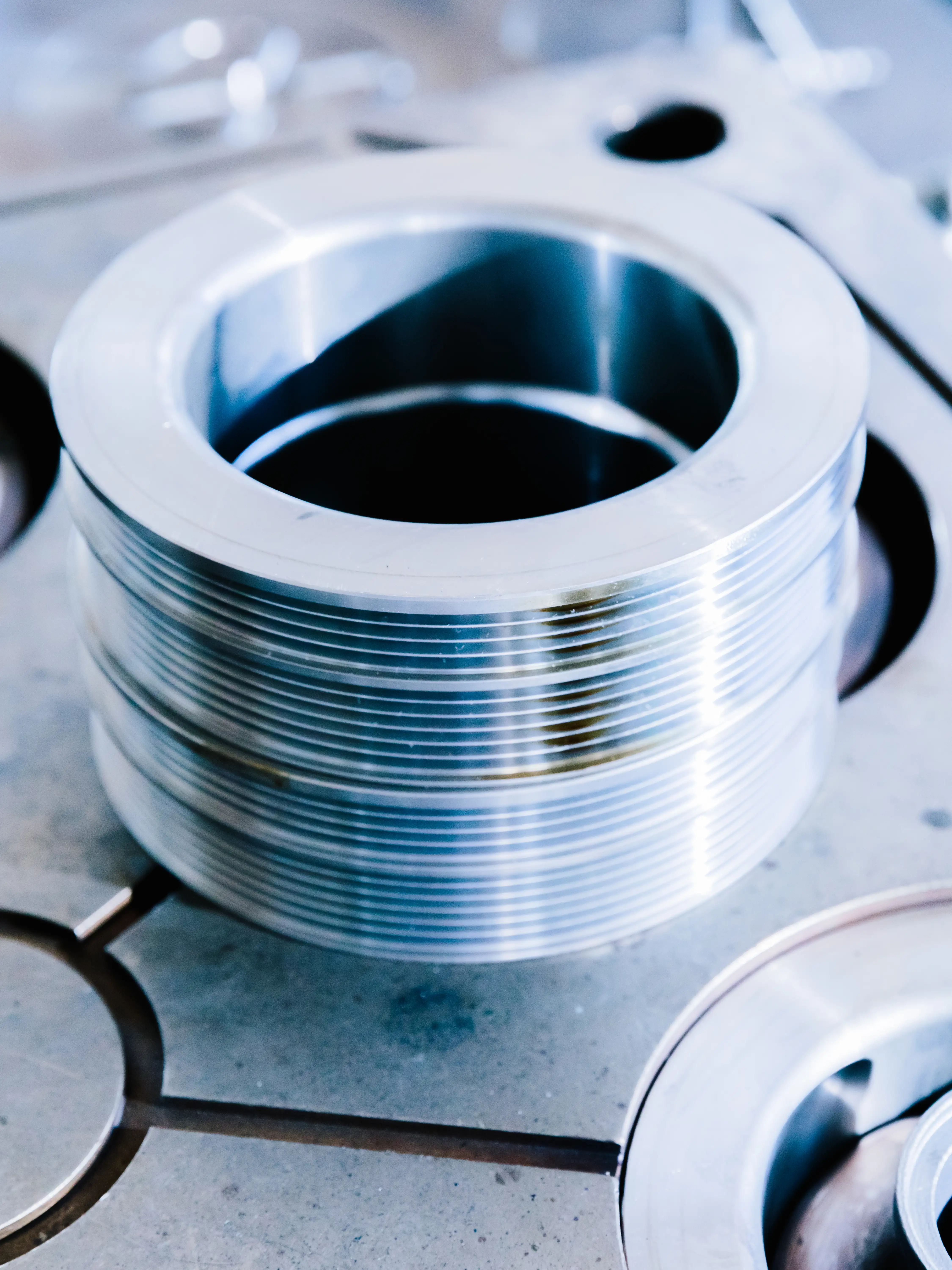 Close-up of a shiny, metallic cylindrical machine part with ridged sides on a metal surface.