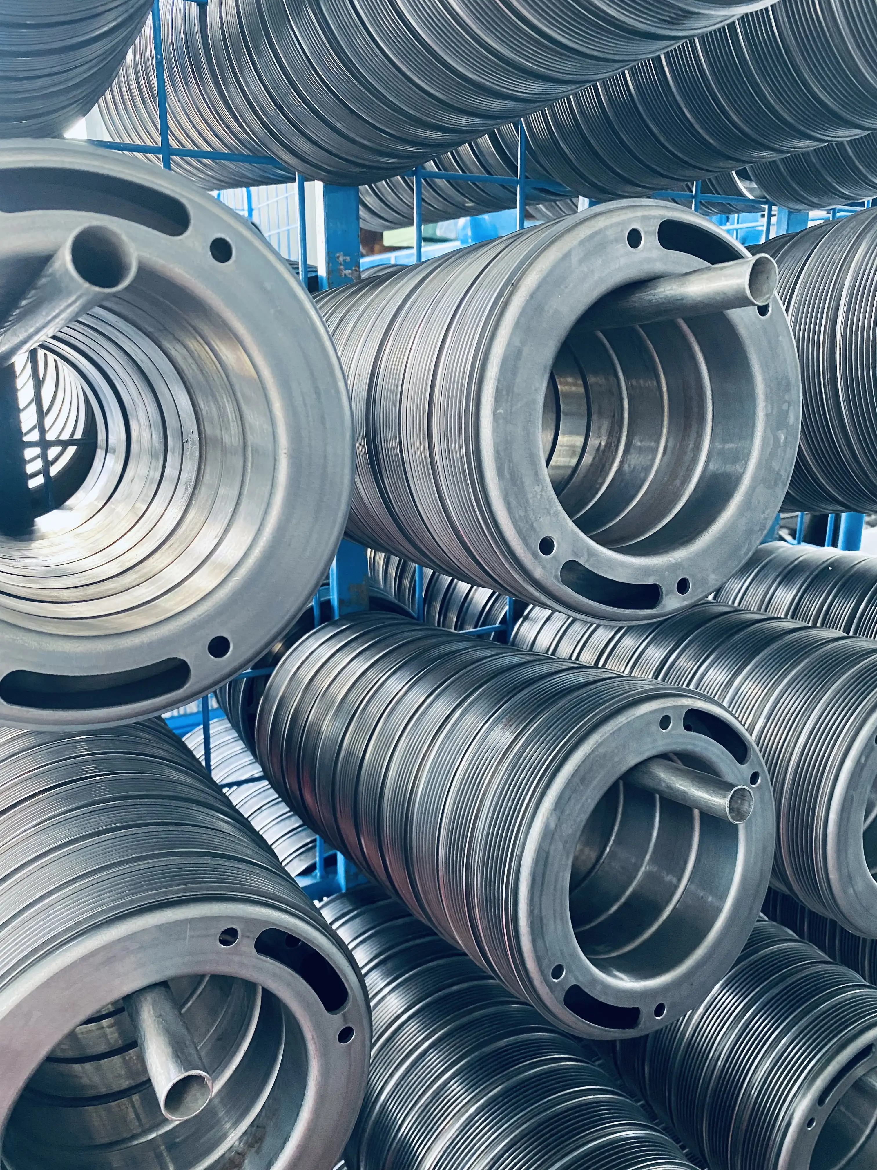 Stacks of coiled metal springs with central rods arranged on blue metal shelves.