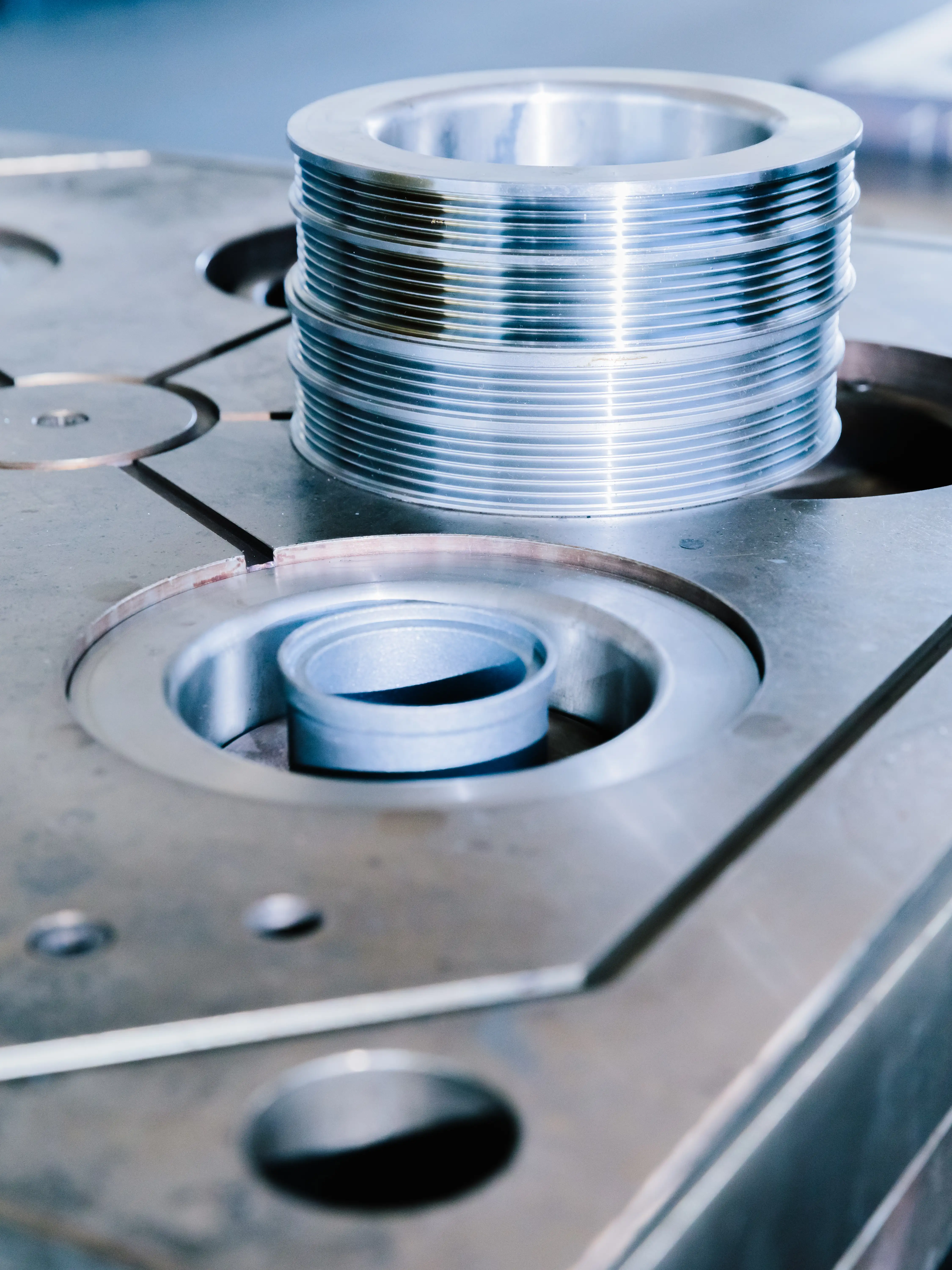 Close-up of shiny metal machine parts with threaded rings and circular slots on a metal surface.