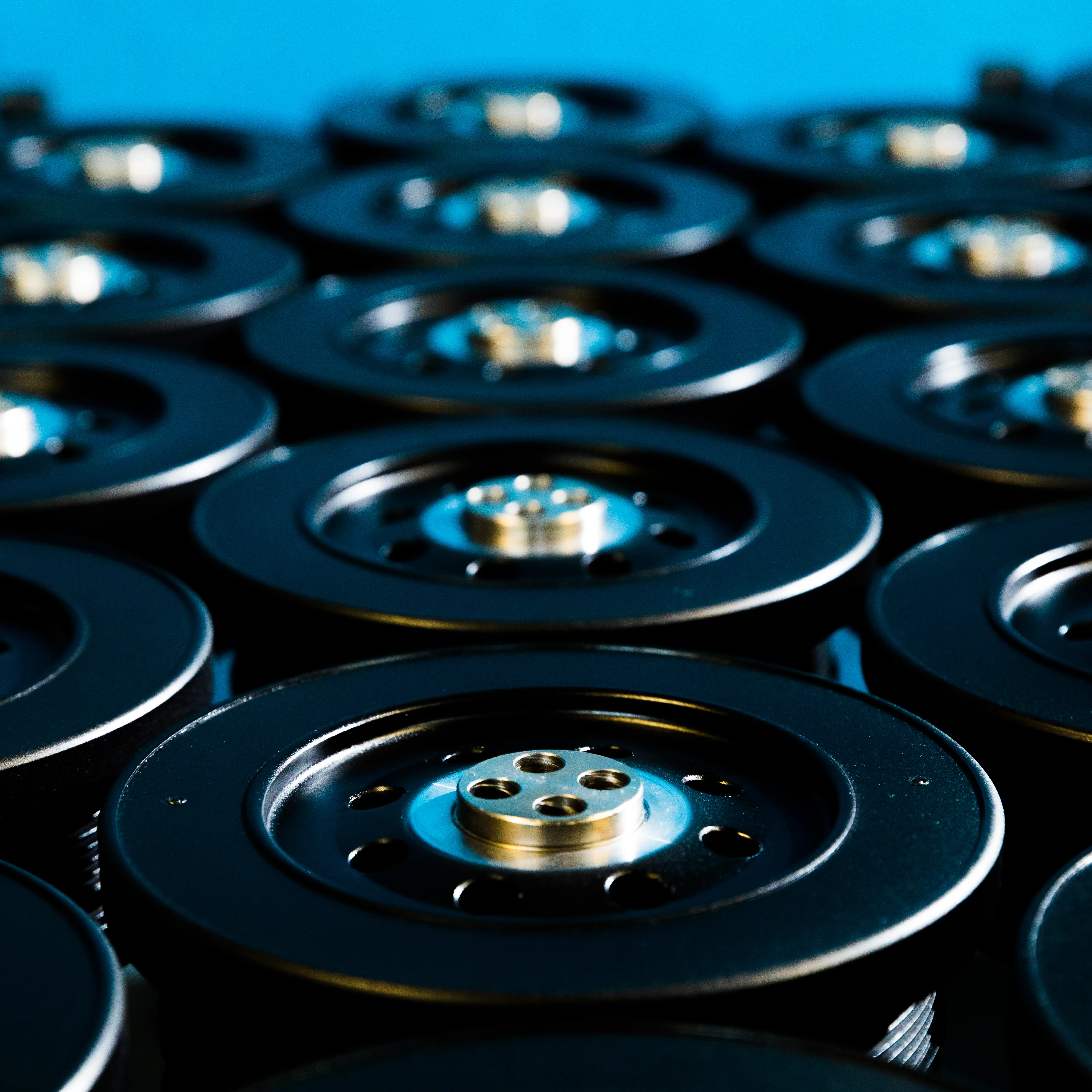Close-up of black machinery parts with metallic centers arranged in rows on a blue background.