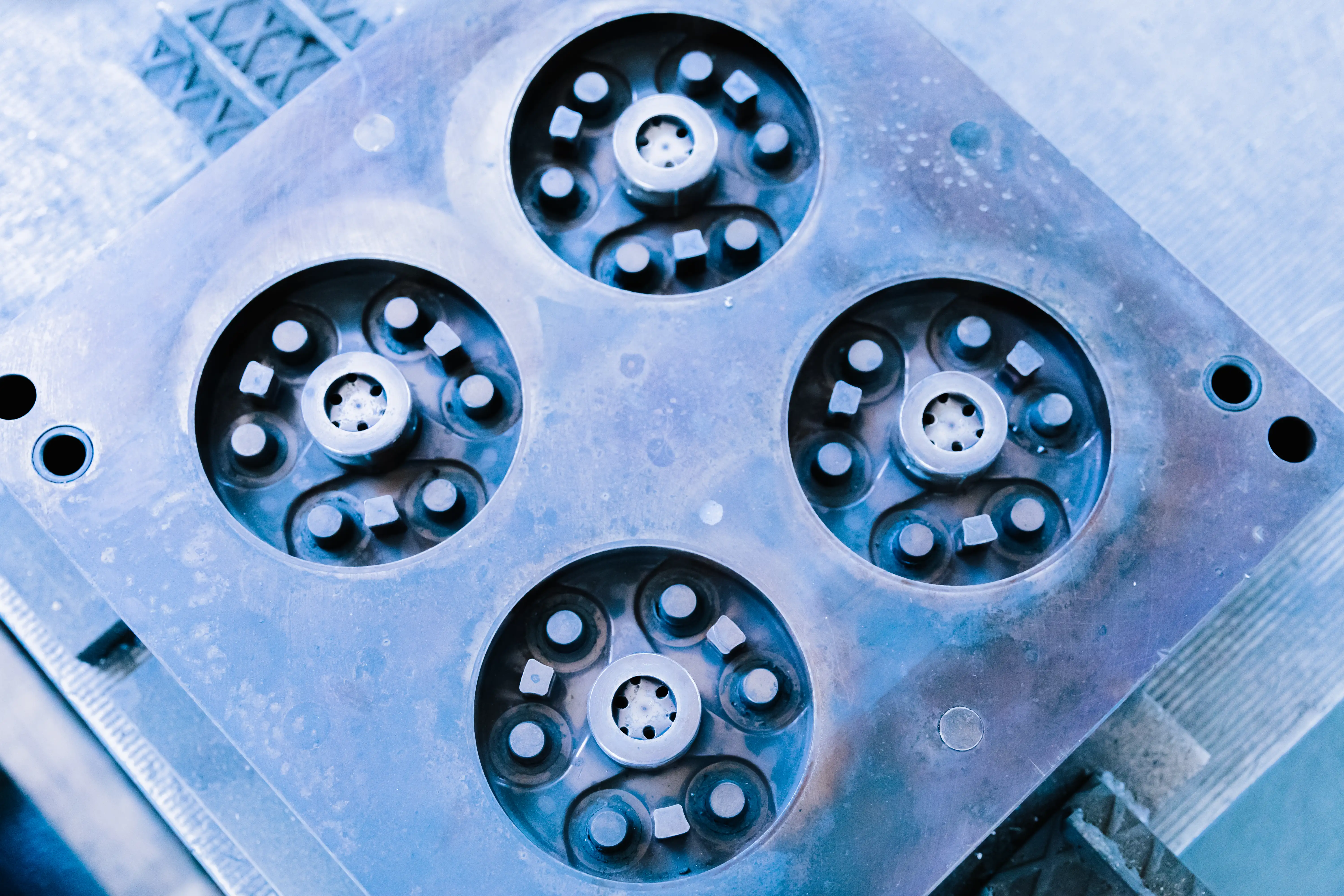 Close-up of a metal industrial mold with four circular cavities containing pins and square pegs.