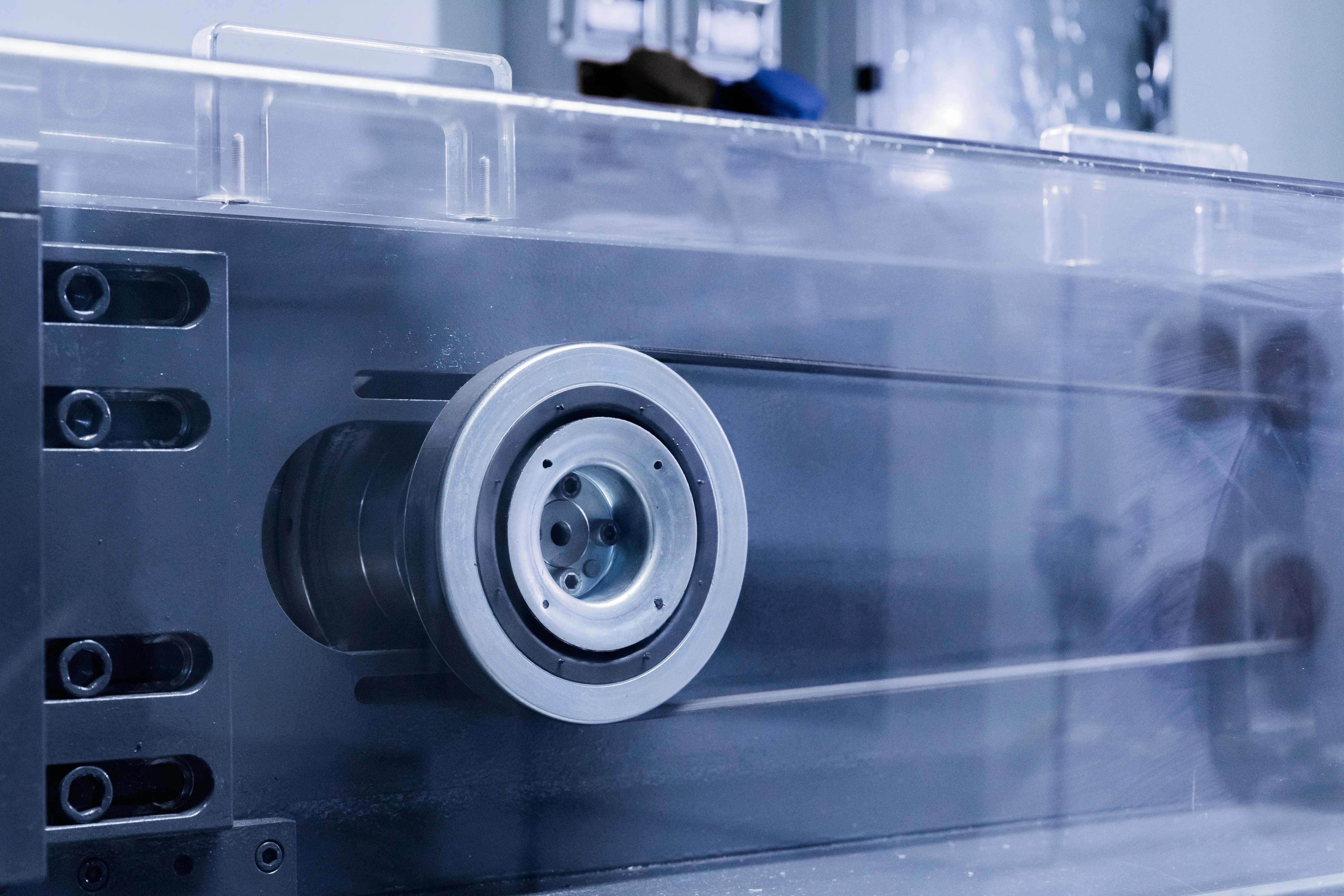 Close-up of a wheel or pulley attached to a metallic industrial machine with transparent guard.