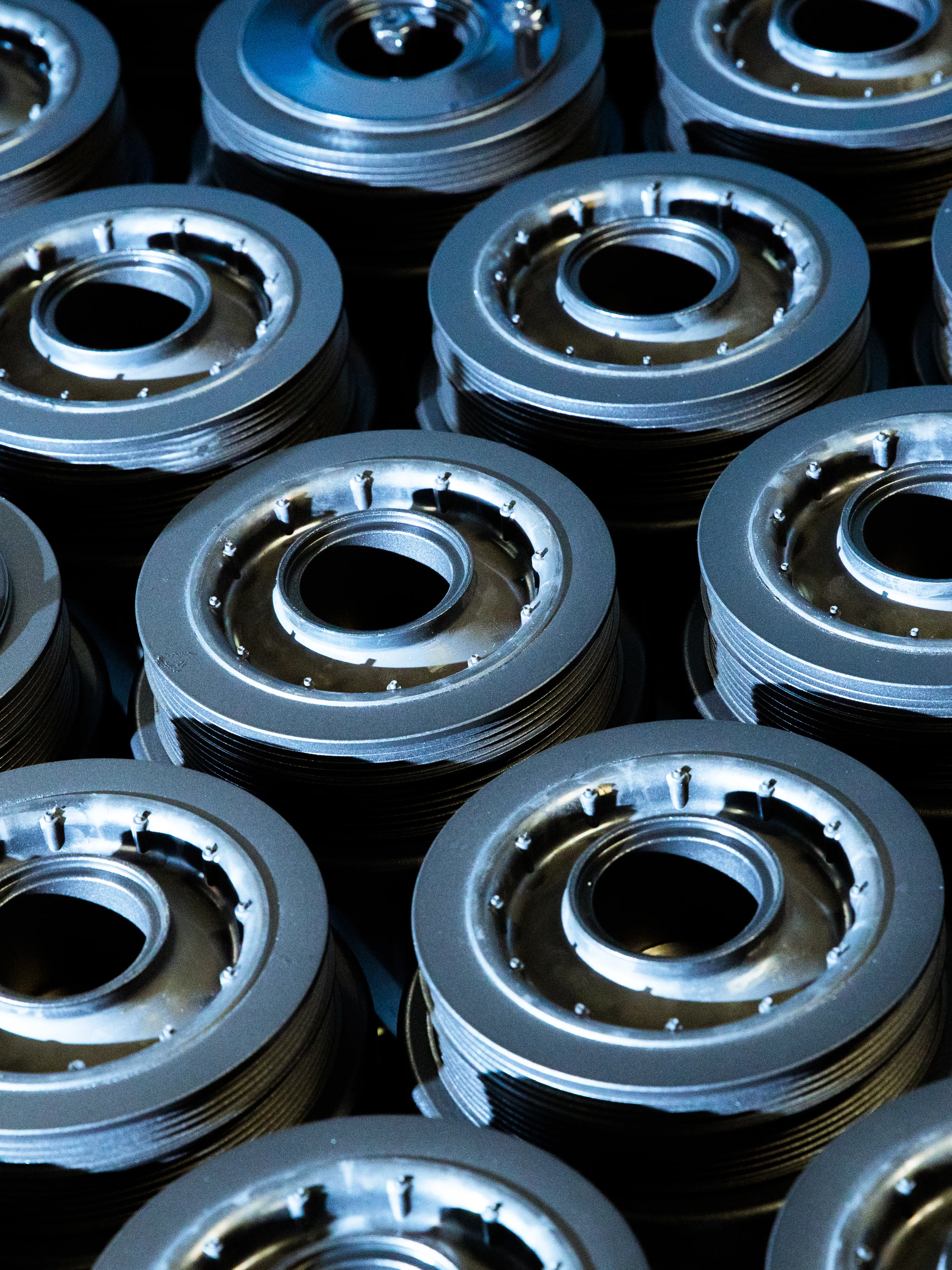 Close-up of stacked metal machine parts with circular openings and grooves under blue lighting.