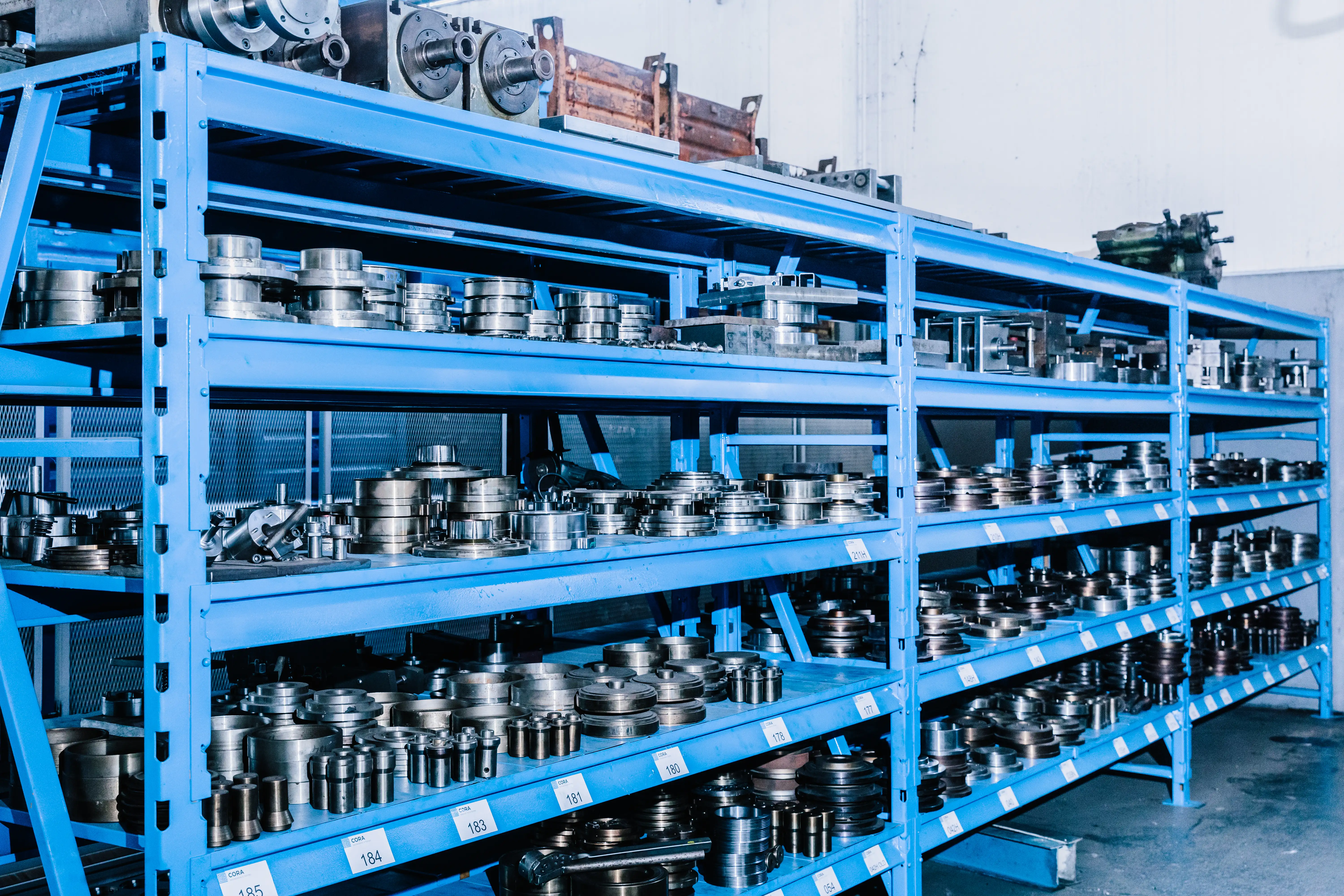 Blue metal shelves filled with organized metal industrial machine parts and tools in a workshop.