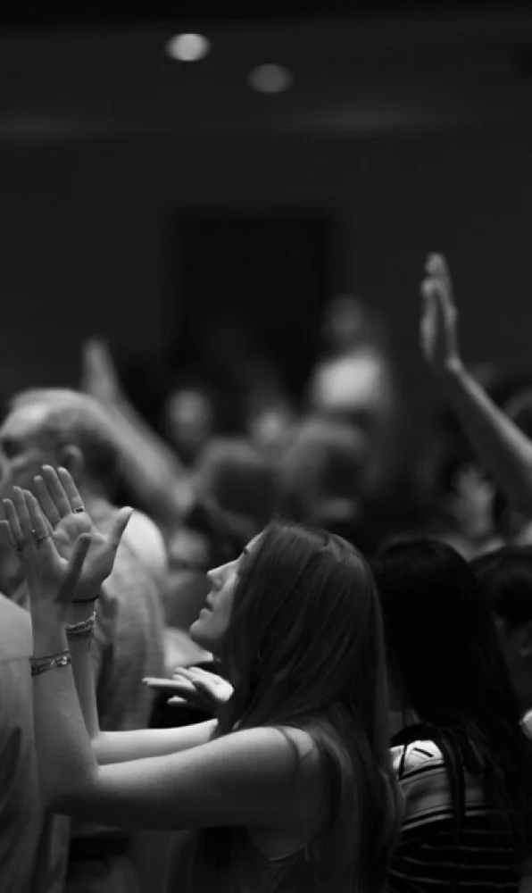 Black-and-white photo of a woman in a crowd with hands raised in worship or praise.