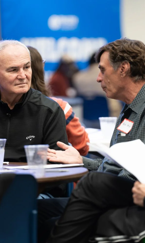 Two middle-aged men having a discussion at a conference table with papers and plastic cups.