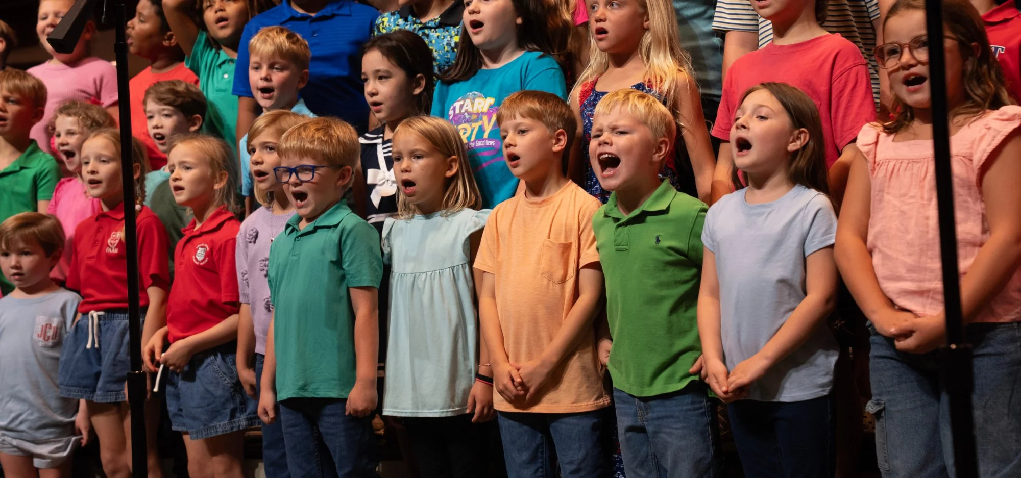Diverse group of children singing together on stage during a choir performance.