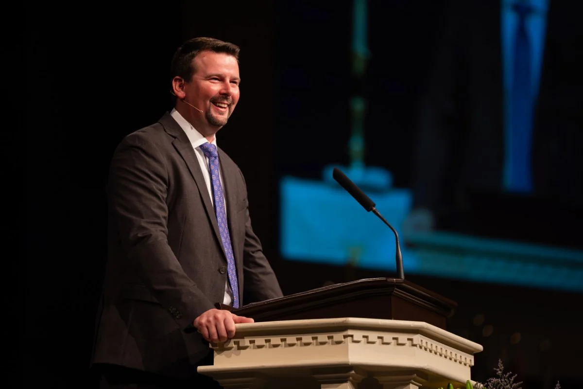 Smiling man in a suit speaking at a podium with a microphone.