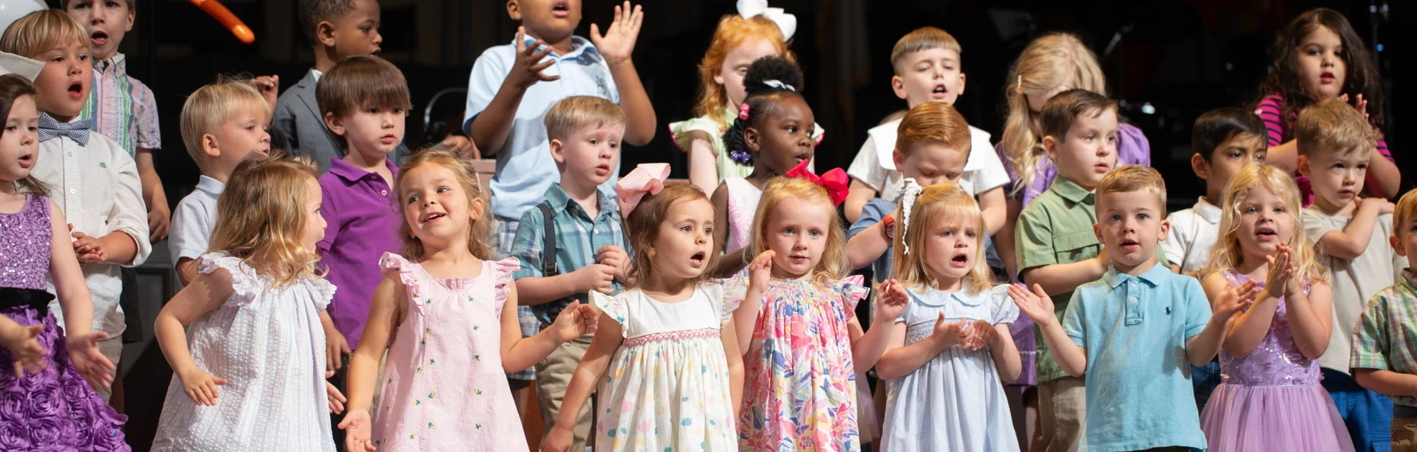 Group of young children singing and clapping on stage during a church performance.