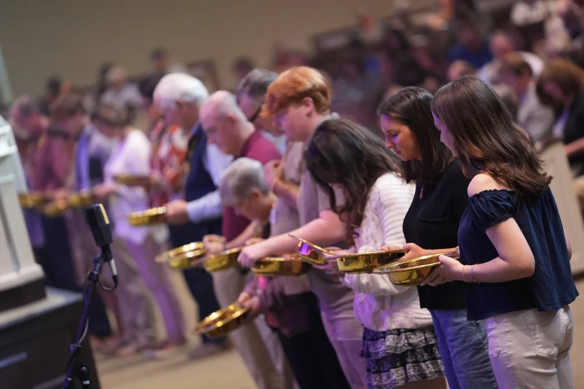 Congregation members lined up holding golden offering plates during a church service.