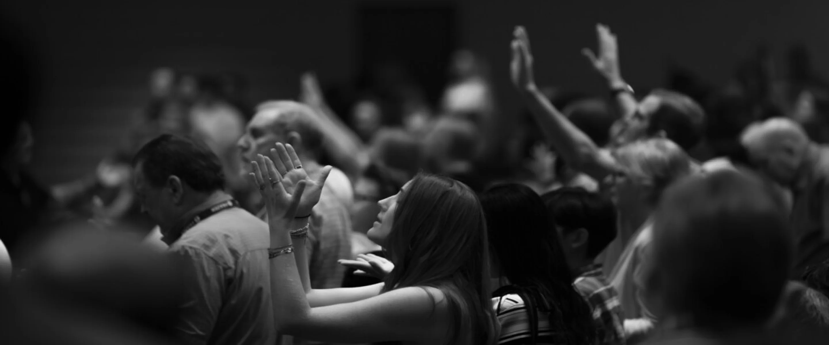 Black and white image of a congregation with raised hands in worship or prayer.