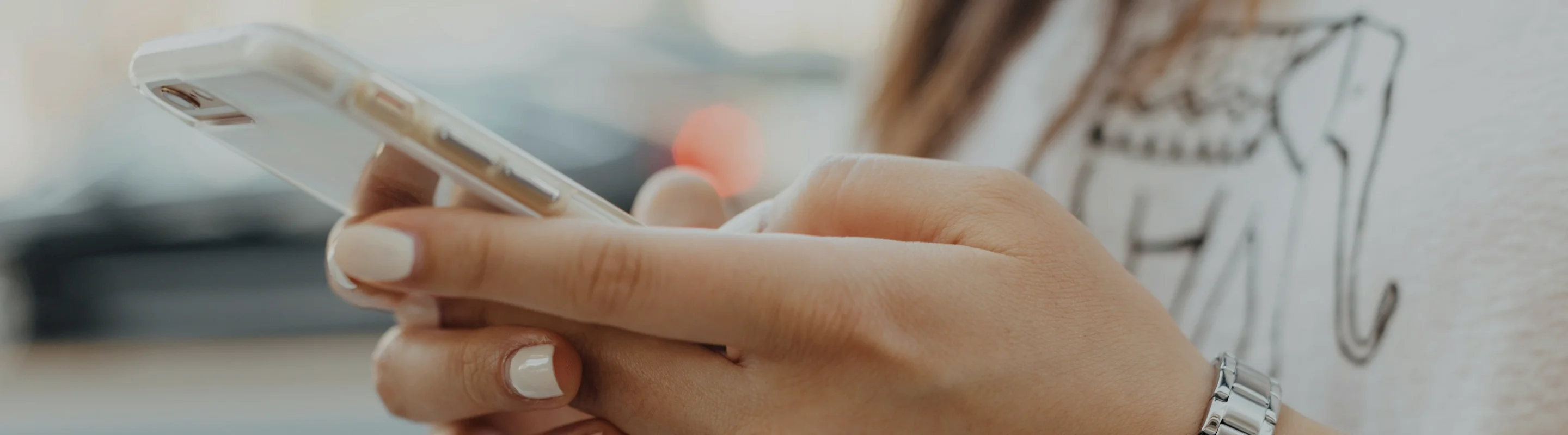 Close-up of a person's hands using a white smartphone, wearing a silver watch and a gray shirt with an elephant design.