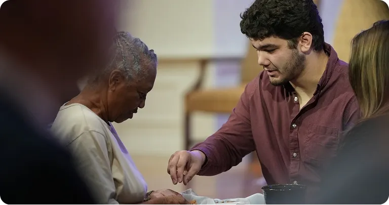 A young man serving communion bread to an elderly woman during a church service.