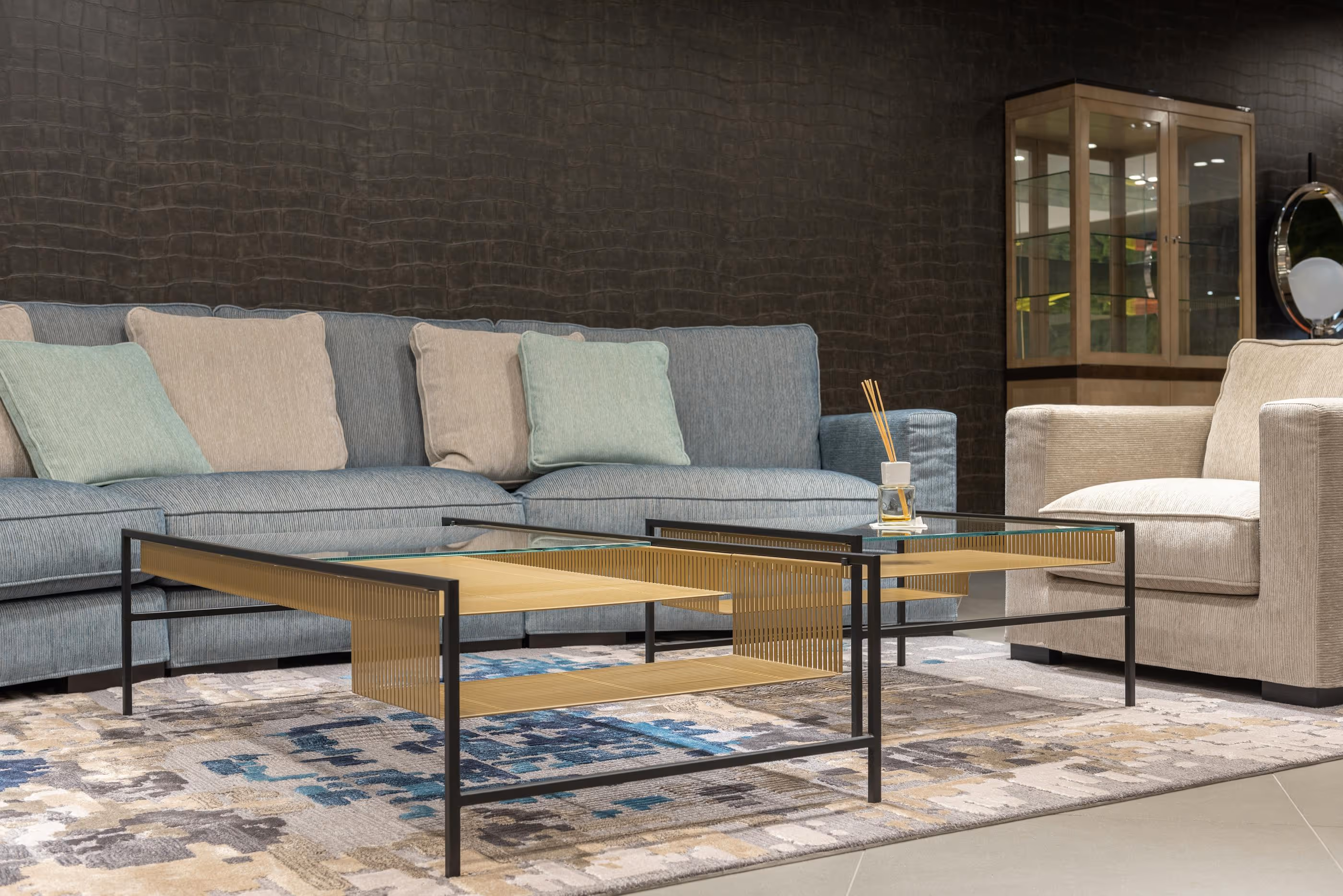 Modern living room with a blue sofa, beige armchair, and glass coffee tables