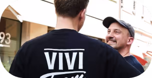 Two men smiling and talking outdoors, one wearing a black shirt with Vivi logo on the back.