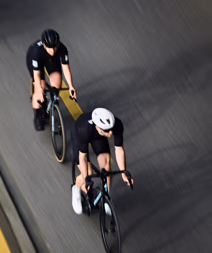 Two cyclists wearing helmets and cycling gear riding on a road with a yellow centerline.