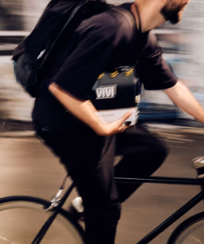 Blurred image of a man wearing black and carrying a backpack while biking and holding a box labeled VIVI.